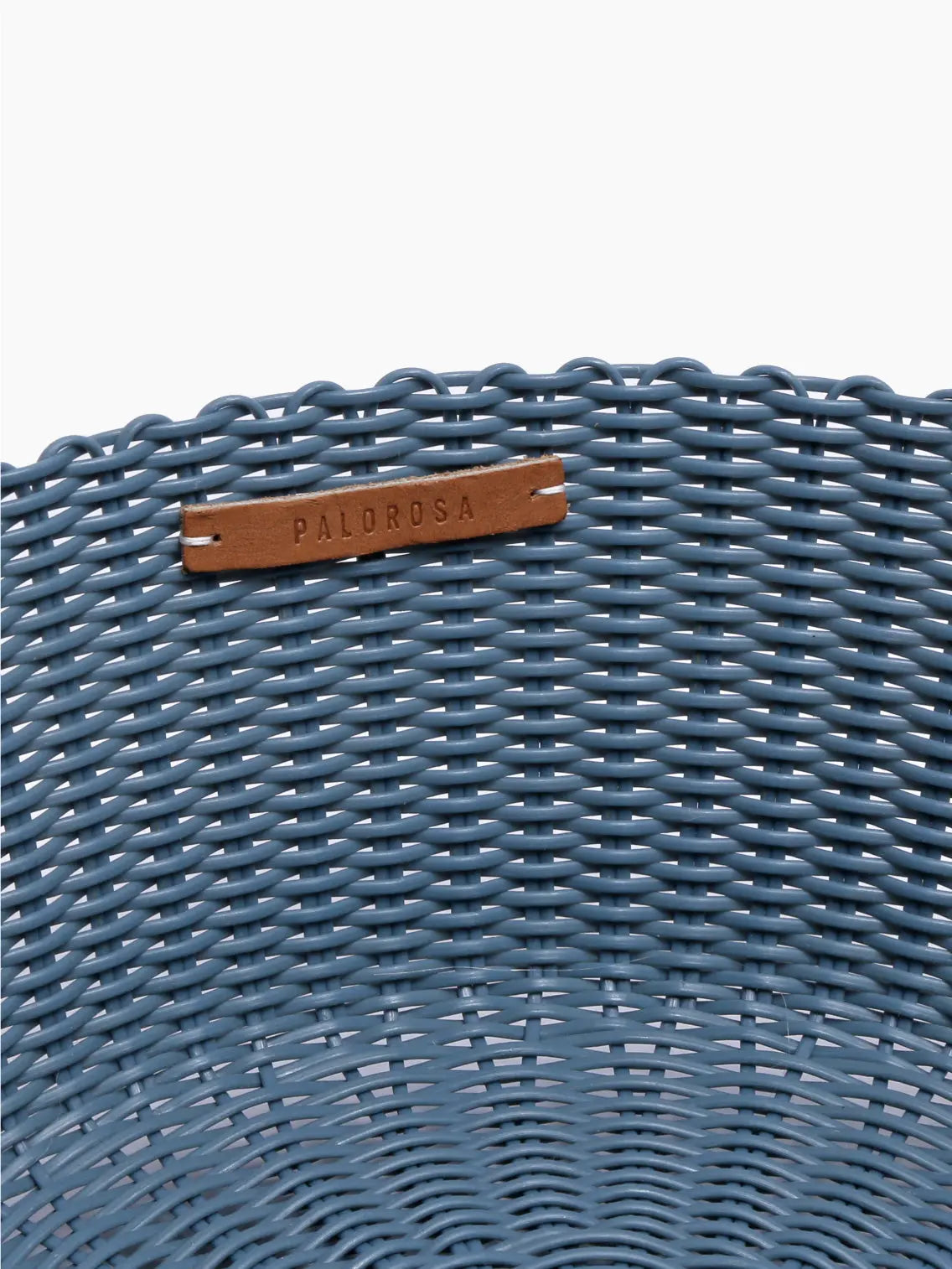A round blue woven storage basket with a textured pattern, perfect to store your essentials. The Fruit Basket Paloblue Small by Palorosa features a small rectangular leather patch stitched on the upper edge. Both the interior and exterior surfaces boast a uniform woven design, available exclusively at Bassalstore in Barcelona.