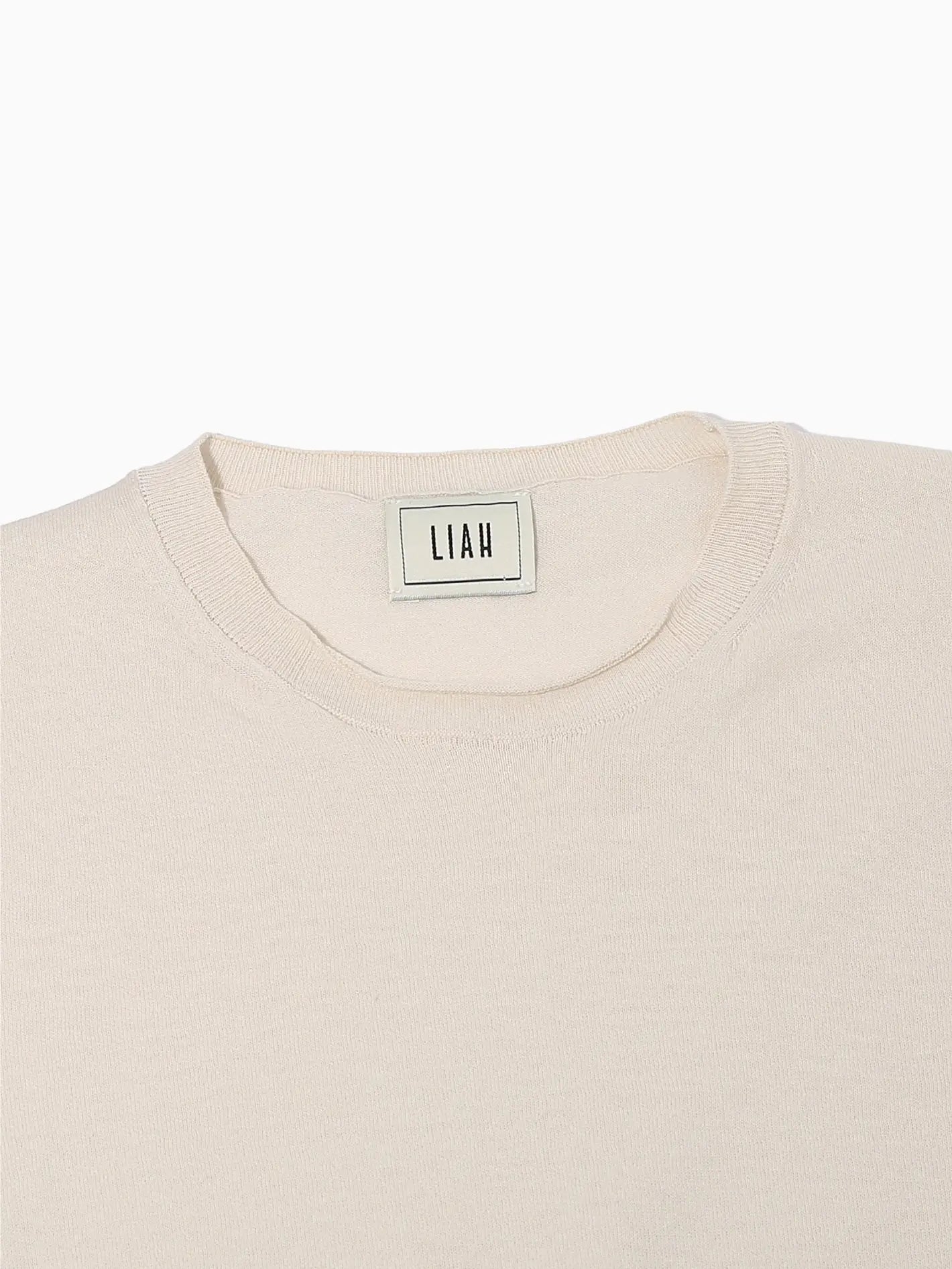A plain beige Gia T-Shirt Ecru from Liah is seen against a white background. The shirt boasts a simple round neckline and a relaxed fit, with subtle stitching visible along the hems of the sleeves and bottom edge, embodying the effortless style of Barcelona.