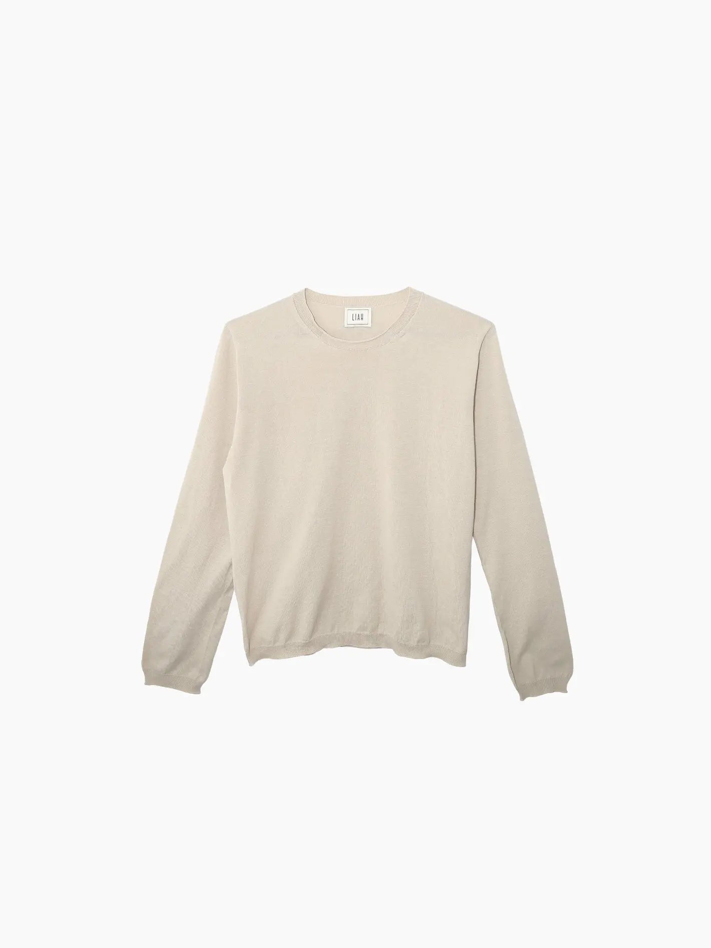 A beige, long-sleeved sweater from Bassalstore is displayed against a plain white background. The Giada T-Shirt Tea from Liah has a minimalist design, featuring a round neckline, ribbed cuffs, and a slightly loose fit. There's a white label with branding at the back of the neckline, reflecting its Barcelona origins.