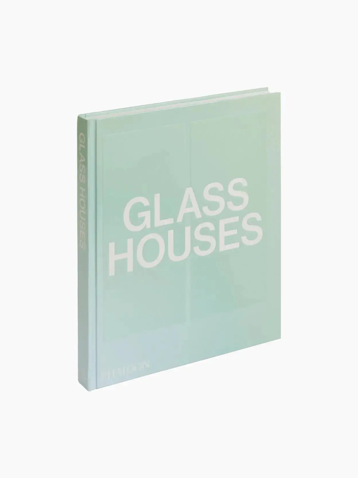 The image shows a light teal hardcover book titled "Glass Houses" tilted slightly backward, displayed in a bassalstore. The text "Glass Houses" is prominently displayed in large white letters on the front cover and spine. The brand name, "Phaidon," appears in smaller white letters at the bottom.