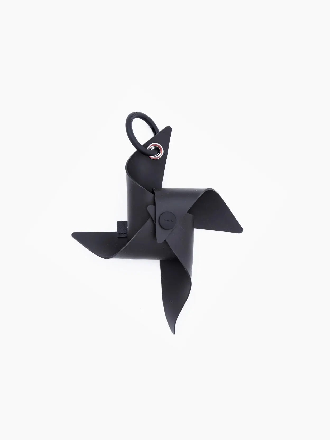 A black, modern pinwheel-shaped object with four blades, centrally fastened and mounted on a small ring, is isolated on a white background. Discover unique items like the Sunnei Gomma Girandola Airpods Holder Black at Bassalstore in Barcelona.
