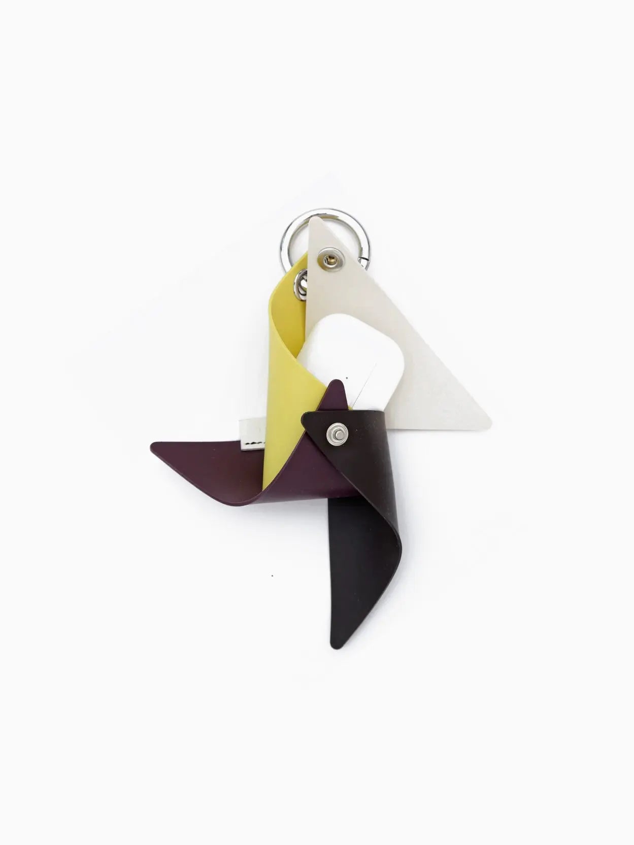 A Gomma Girandola Airpods Holder Multi Off White by Sunnei designed to resemble a pinwheel with four blades, colored yellow, white, dark purple, and dark brown. The metal keyring is attached at the top. This stylish accessory can be found at Bassalstore in Barcelona. The entire design sits against a plain white background.