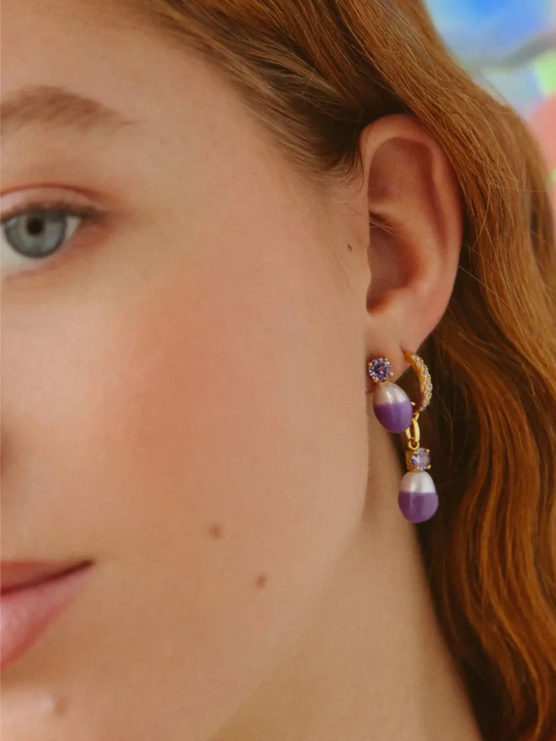 A single gold earring adorned with small diamonds along the hoop. The Grape Swan Lake Pearl Hoop Earring by Wilhelmina Garcia, available at Bassalstore in Barcelona, features a dangling purple gemstone above a purple and white bead.