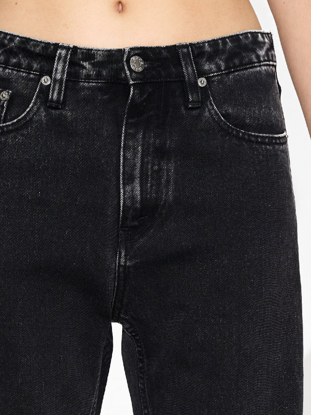 A person wearing Hope's Easy Jeans Chipped Black, high-waisted and loose-fitting, made from sustainable denim and paired with black shoes, stands with arms relaxed by their sides against a white background. These jeans, crafted from organic cotton, feature front pockets, belt loops, and a button/zipper closure. The person's torso is not shown.