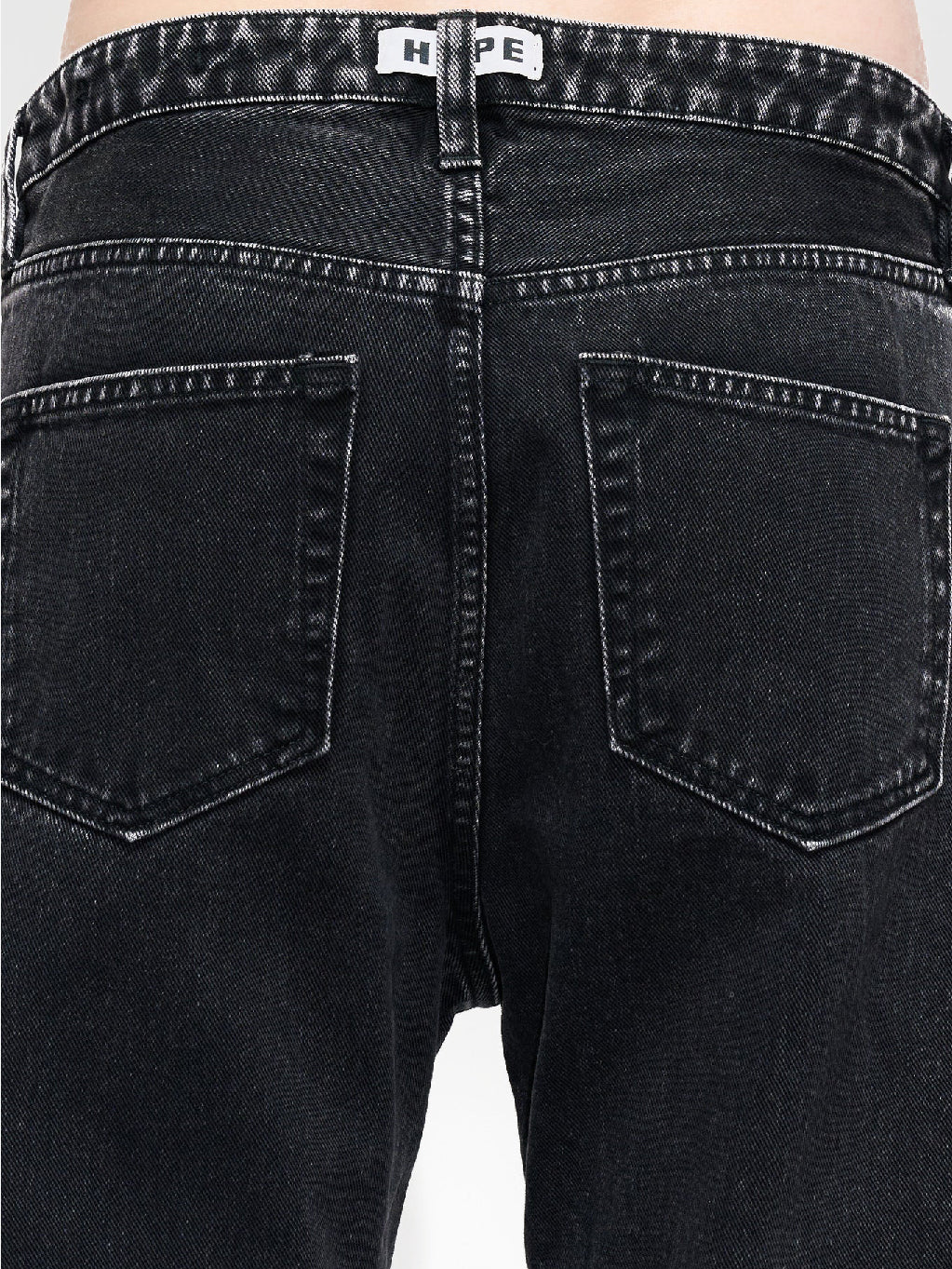 A person wearing Hope's Easy Jeans Chipped Black, high-waisted and loose-fitting, made from sustainable denim and paired with black shoes, stands with arms relaxed by their sides against a white background. These jeans, crafted from organic cotton, feature front pockets, belt loops, and a button/zipper closure. The person's torso is not shown.