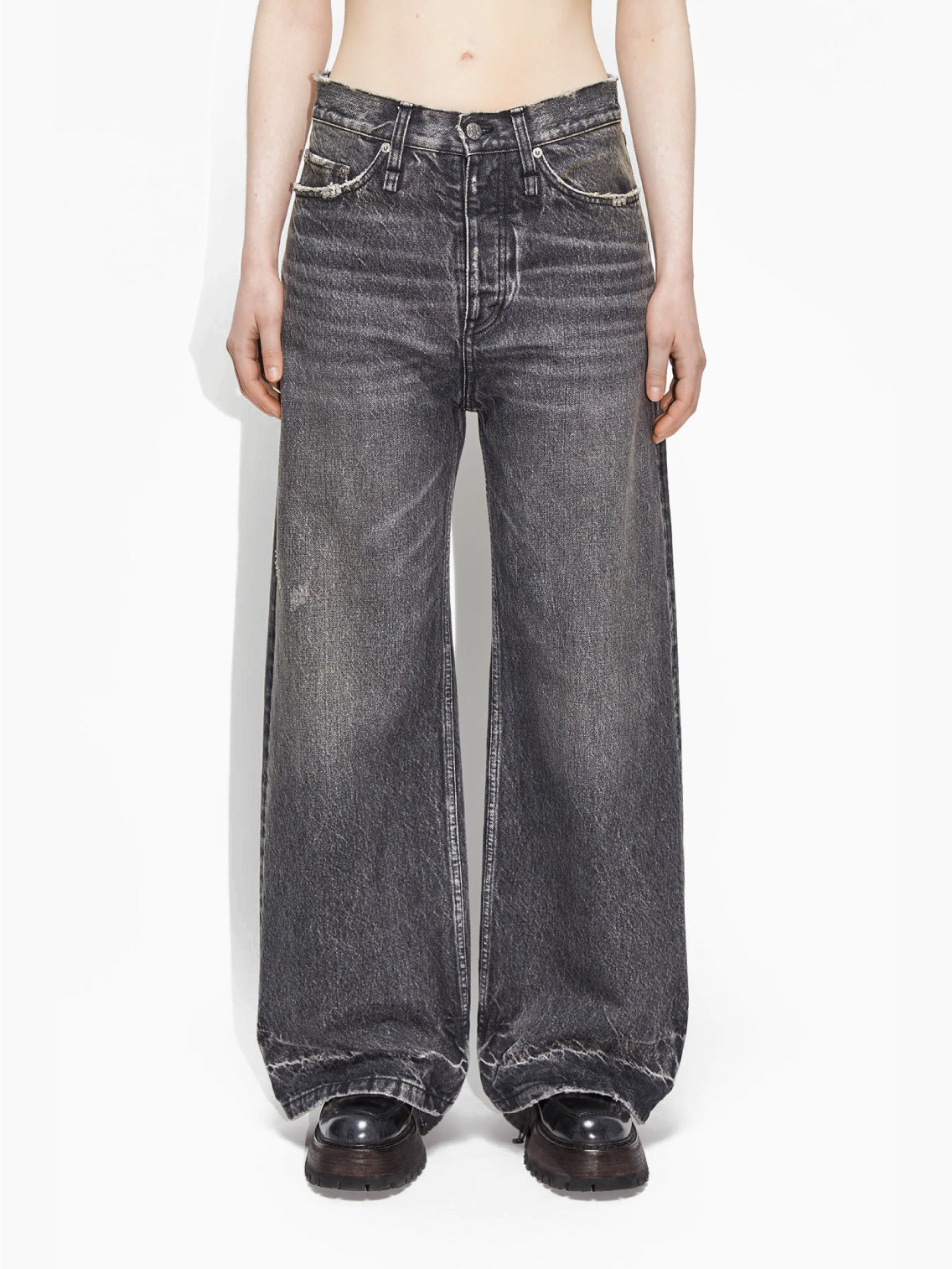 A person wearing Hope's Skid Jeans Heavy Black Vintage, which are loose-fitting and high-waisted with a slightly frayed hem. They are also sporting black shoes, while their upper body and head remain out of the frame against a plain white background.