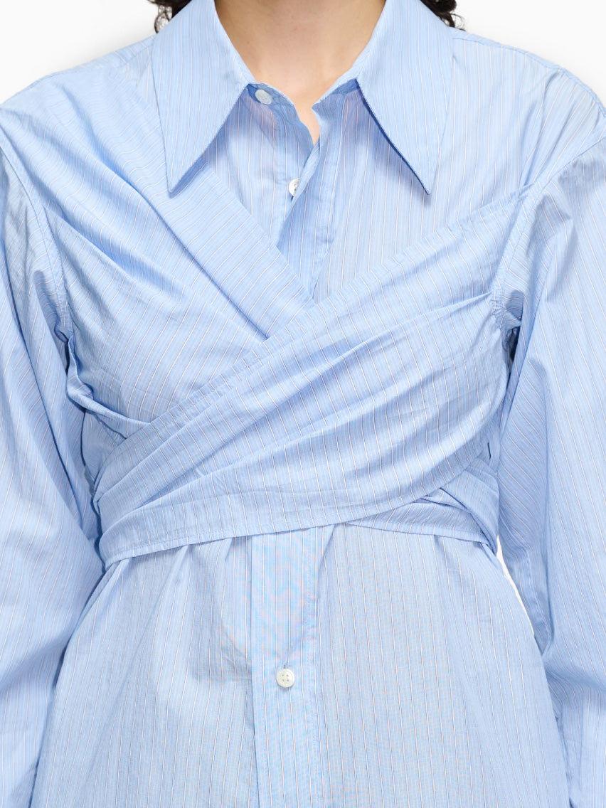 The Twisty Shirt Office Blue Stripe from Hope is crafted from striped cotton fabric in a light blue hue. This long-sleeved shirt features buttons down the front, a waist tie detail, and an oversized, structured collar for a chic touch.