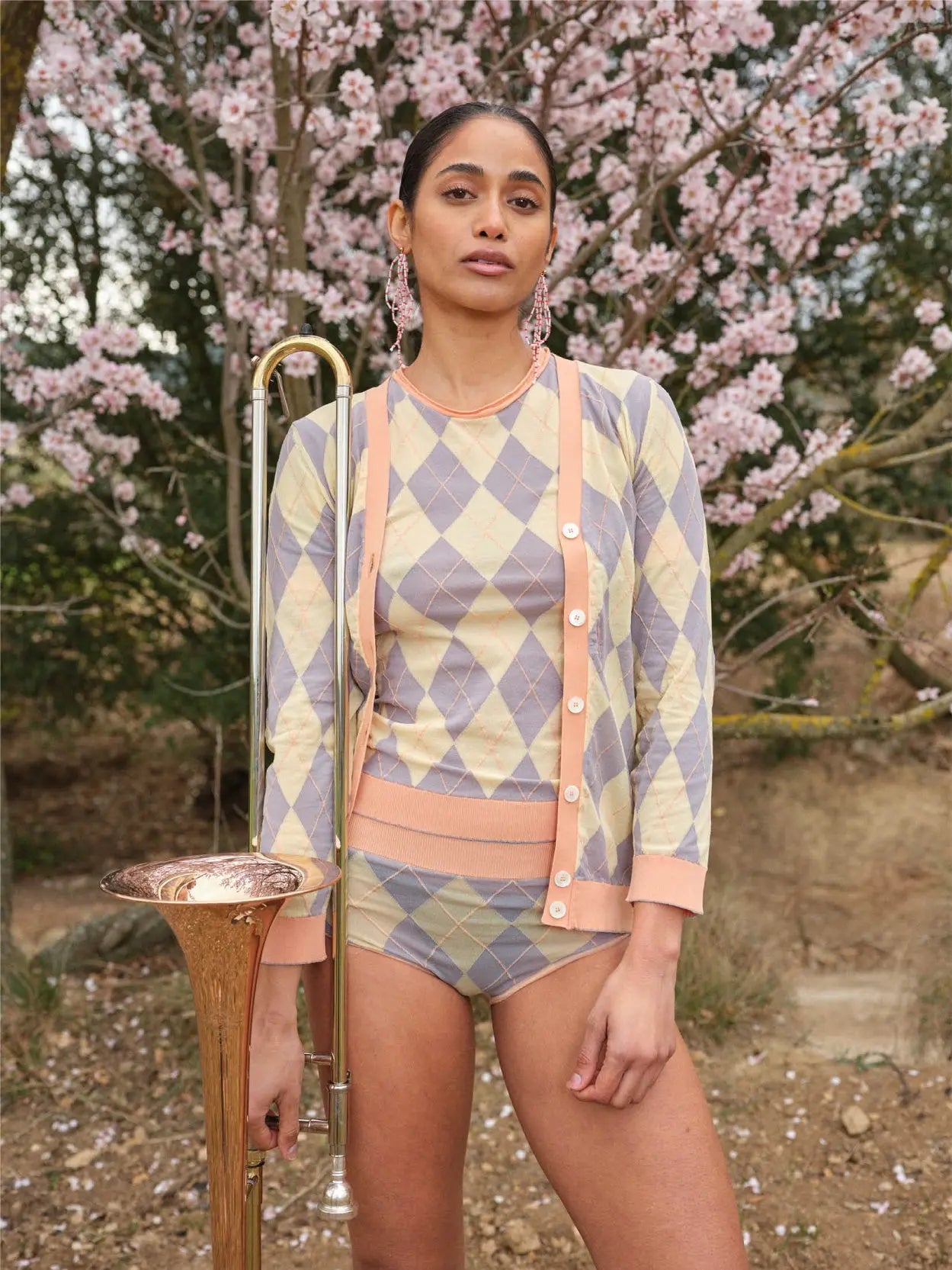 A short-sleeve sweater with a pastel argyle pattern featuring diamond shapes in light yellow and blue on a beige background. The Jes Sweater Peach by Bielo, available at Bassalstore in Barcelona, has light pink ribbed cuffs at the sleeves, neckline, and hem.