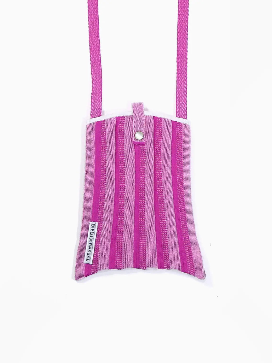 A small, rectangular Lilac Shoulder Bag with vertical pink and purple stripes. It has a snap button closure on top, and the strap is of the same material and color scheme. A small white tag with text from Bielo x Bassal Store is sewn on one side of the bag. The background is white.