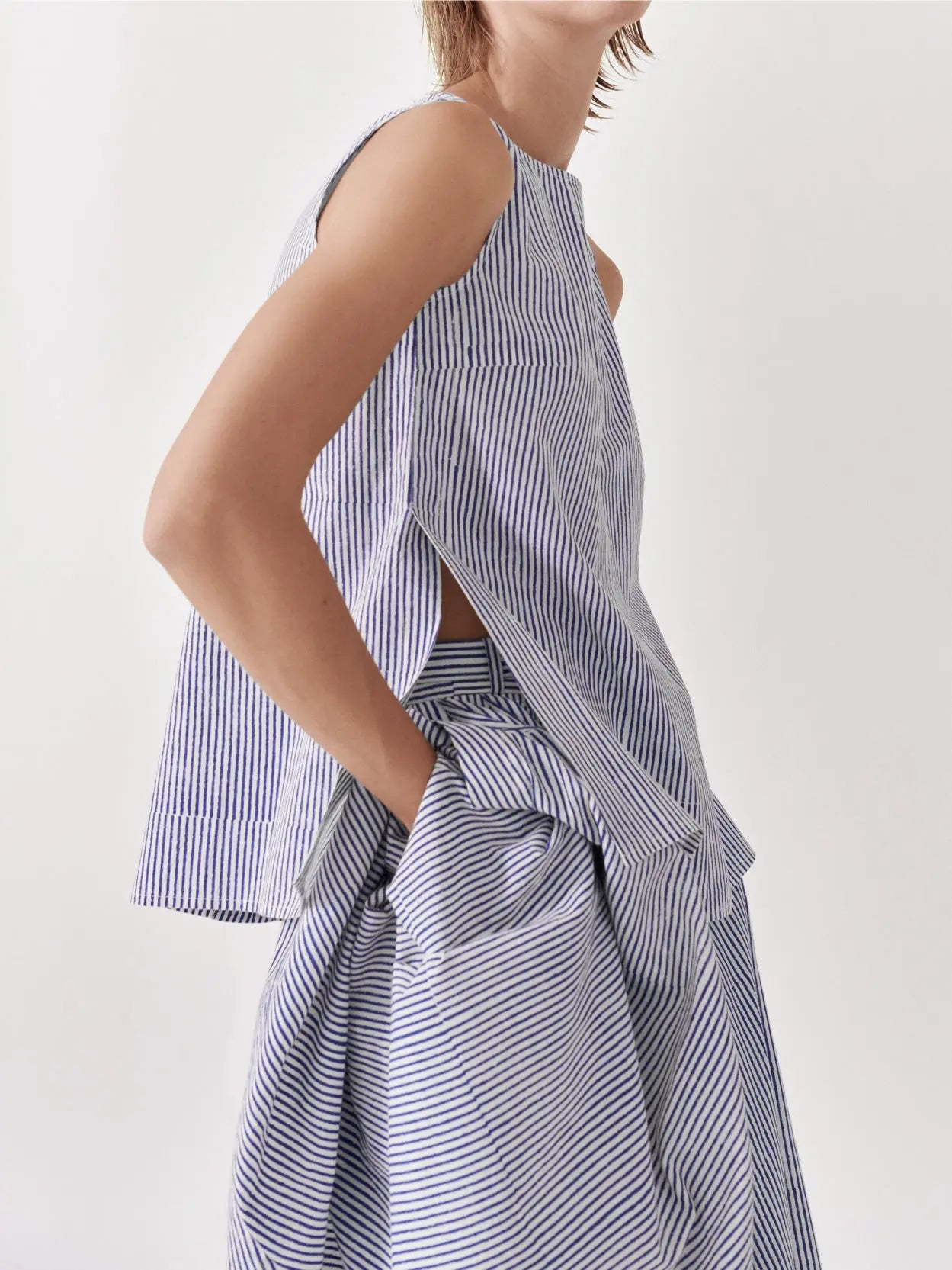 A sleeveless, blue and white vertical striped blouse is displayed on a plain white background. The Louise Top Block Print Stripe by Jan Machenhauer, available at Bassalstore in Barcelona, has a loose fit with a round neckline and a subtle, casual design.