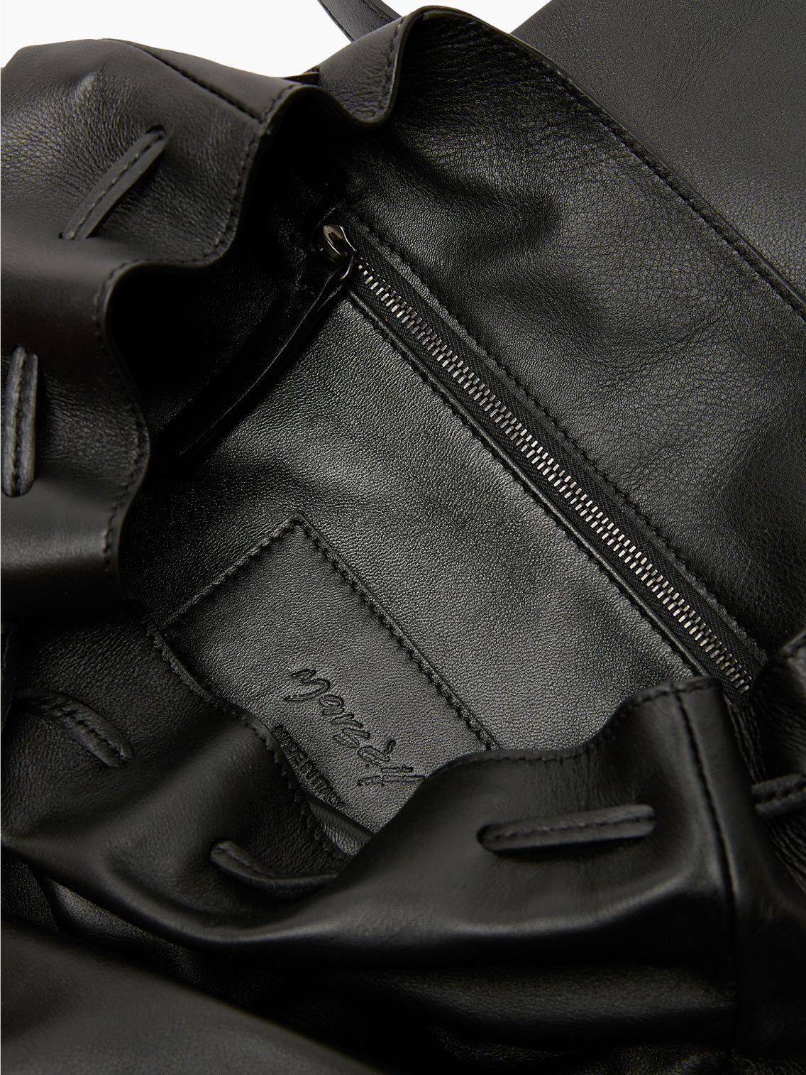 The Pattina Backpack Black by Marsèll is a black leather backpack featuring a flap-top closure and a handle at the top. Crafted with contemporary style, the front of the flap showcases a subtle embossed logo. Made in Italy, this sleek and minimalist design seamlessly blends elegance with functionality.