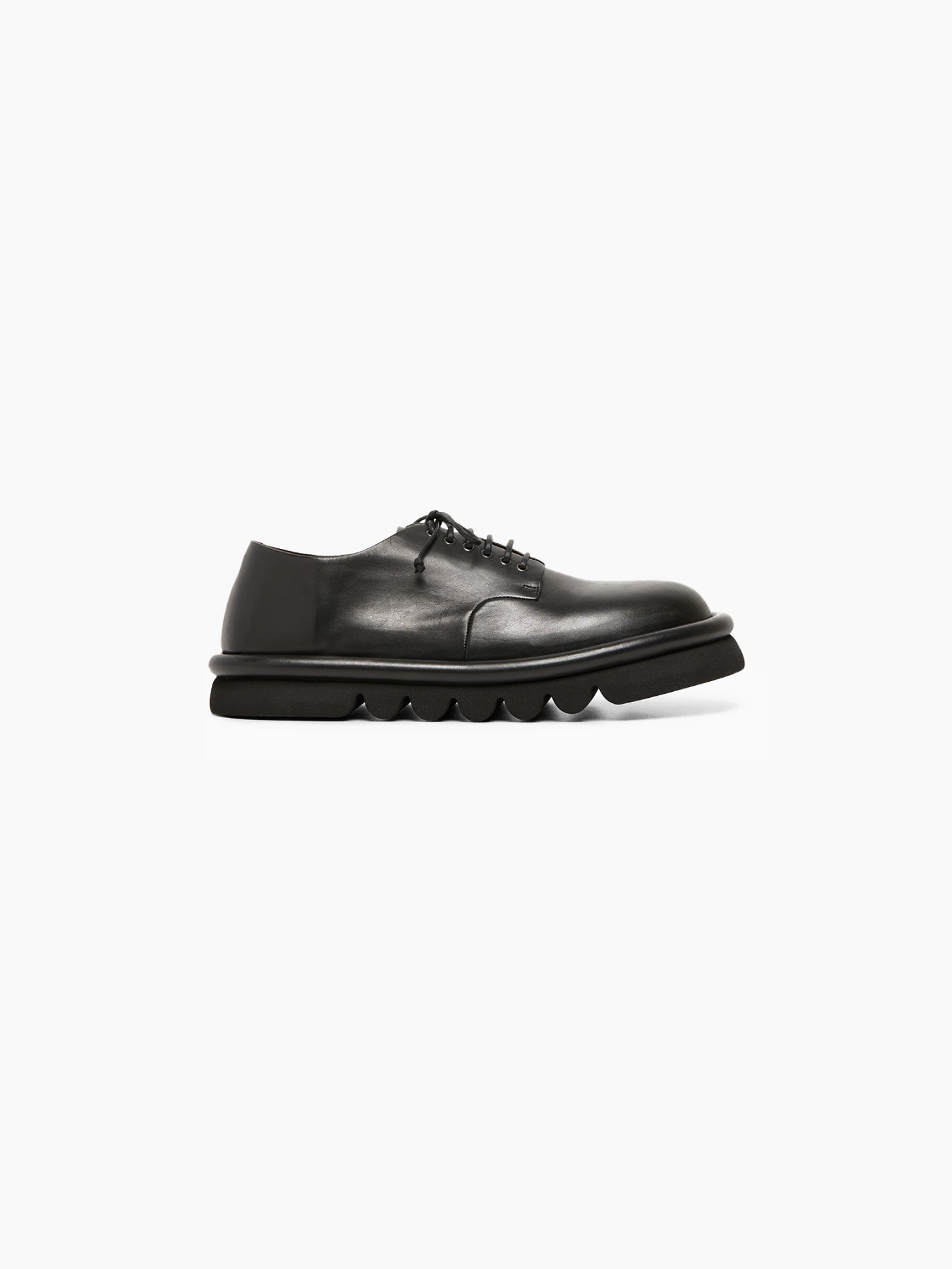 The Marsèll Tonde Derby Shoe in black is showcased individually against a white background. This Italian-made shoe features black leather, matching black laces, and a chunky, textured black sole. It boasts a sleek, minimalist design with a polished and pristine appearance.