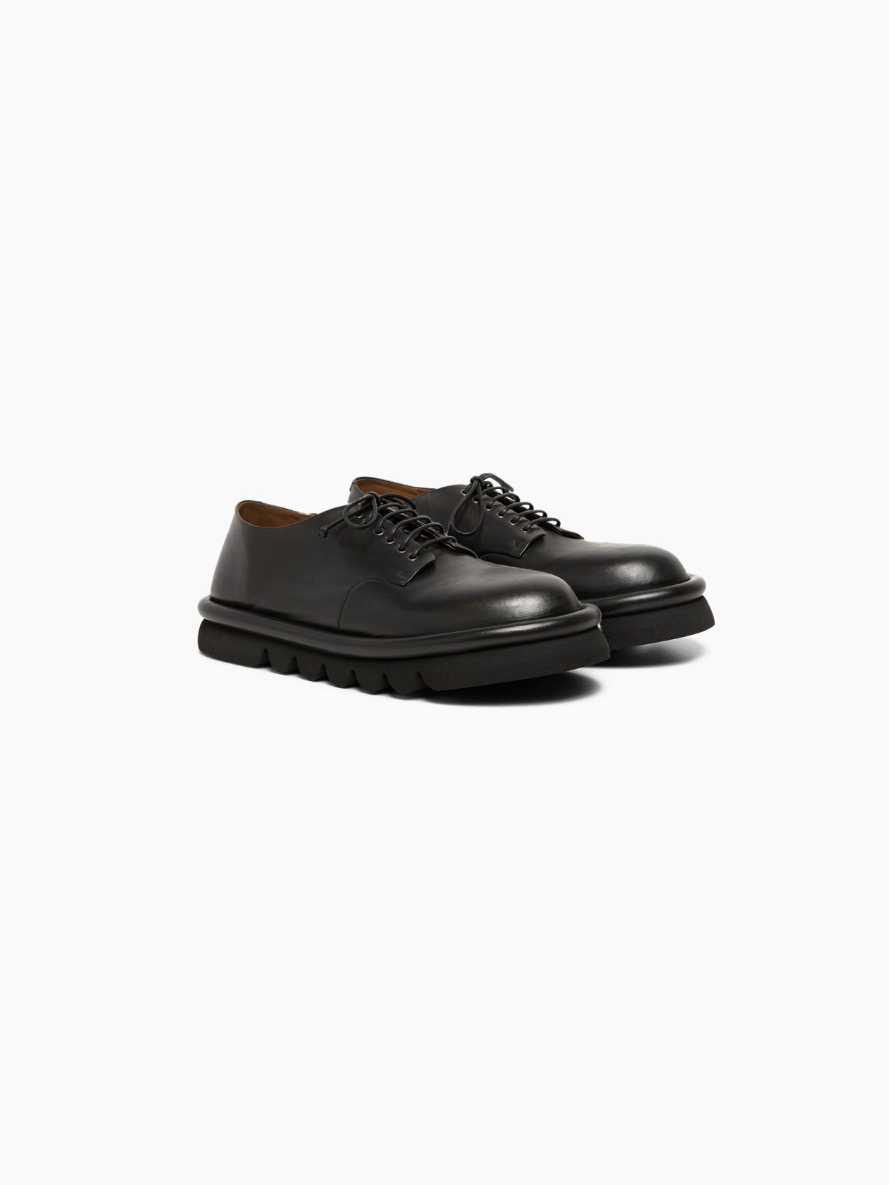 The Marsèll Tonde Derby Shoe in black is showcased individually against a white background. This Italian-made shoe features black leather, matching black laces, and a chunky, textured black sole. It boasts a sleek, minimalist design with a polished and pristine appearance.