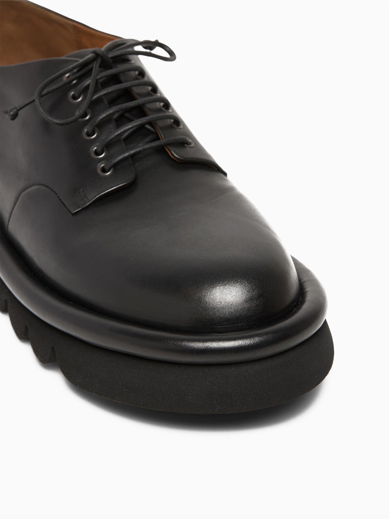 The Marsèll Tonde Derby Shoe in black is showcased individually against a white background. This Italian-made shoe features black leather, matching black laces, and a chunky, textured black sole. It boasts a sleek, minimalist design with a polished and pristine appearance.