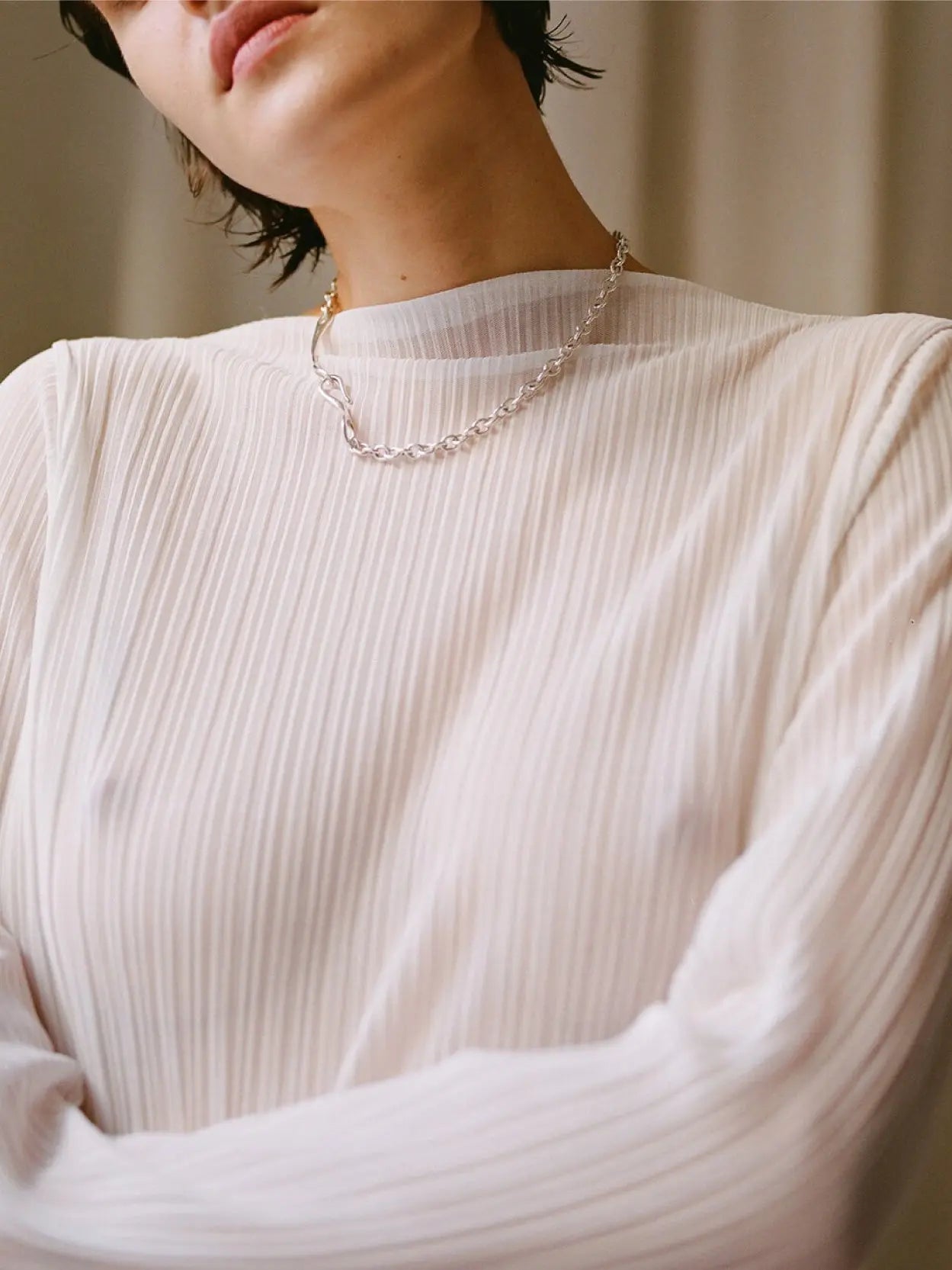 A Maia Necklace from Nathalie Schreckenberg, featuring a linked chain design with a small heart-shaped clasp, laid out in an oval shape on a white background.