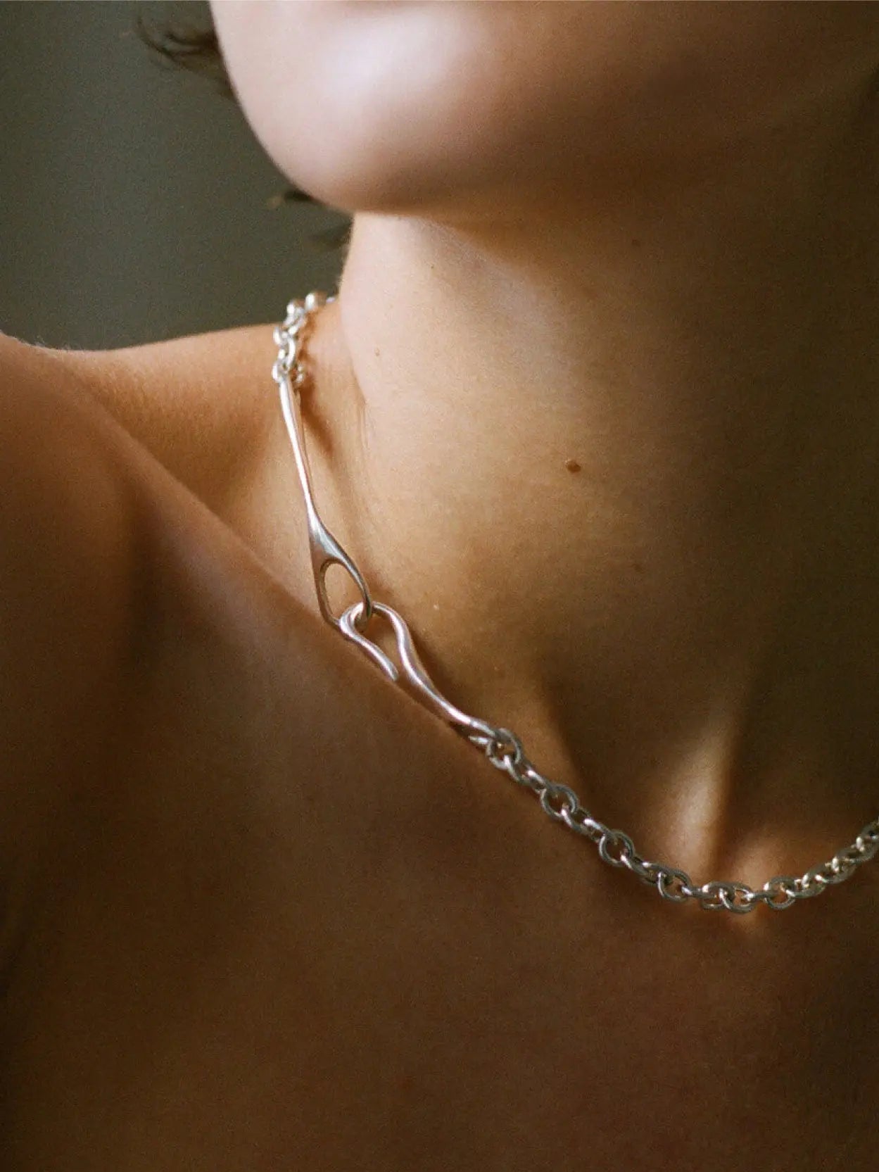 A Maia Necklace from Nathalie Schreckenberg, featuring a linked chain design with a small heart-shaped clasp, laid out in an oval shape on a white background.