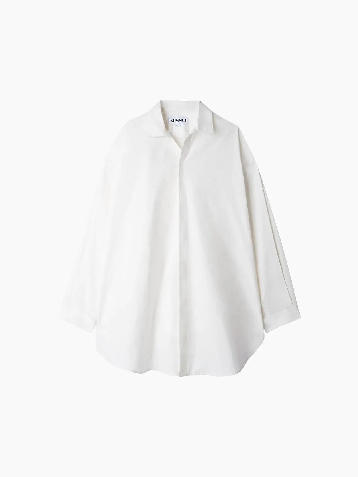 A white button-up shirt with long sleeves, a collar, and a loose, slightly oversized fit. The Mega Overshirt White has a minimalist design and appears to be made from lightweight fabric. A small tag with text is visible at the back of the collar, subtly nodding to its origins from Sunnei in Barcelona.