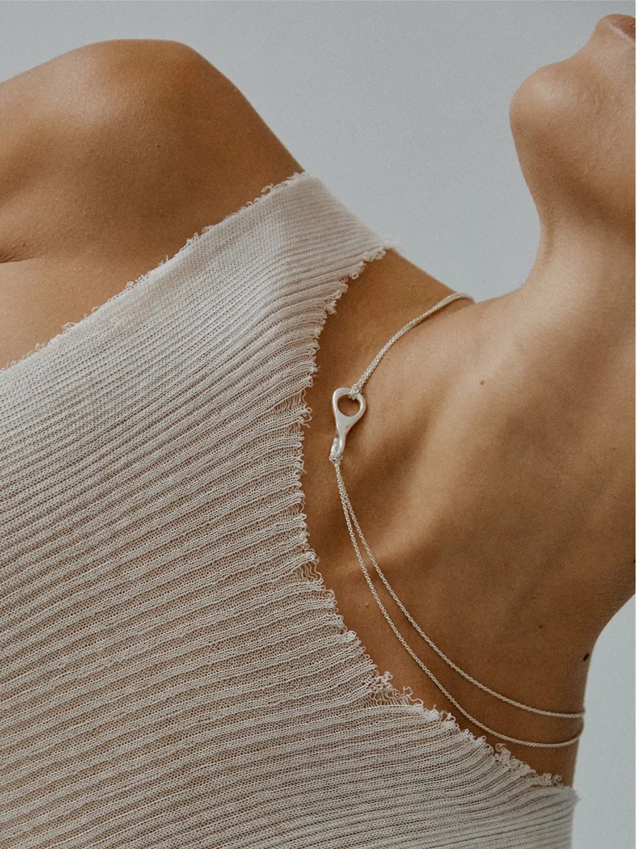 A delicate Mel Double Chain Necklace from Nathalie Schreckenberg, featuring a small, intricately designed clasp, is shown against a plain white background. The thin chain forms a slight curve, highlighting its simplicity and elegance.