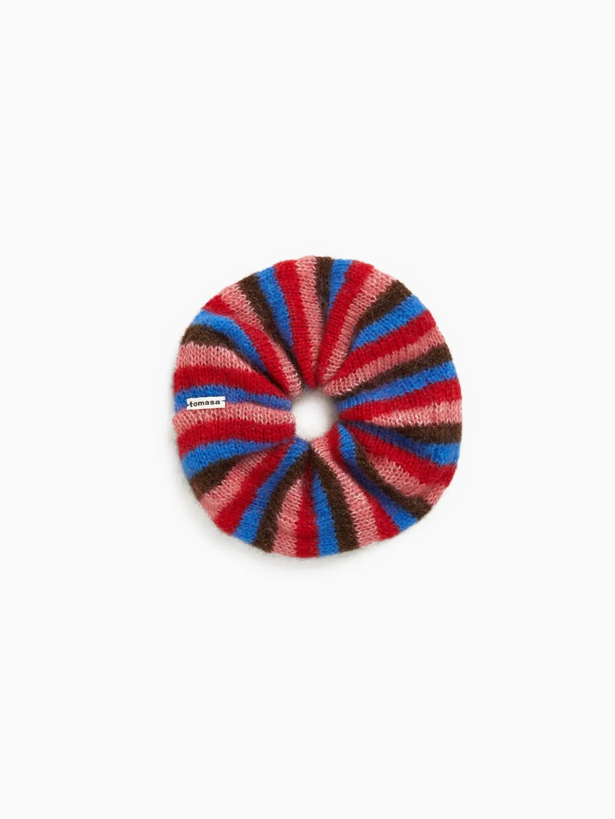 A round, knitted Mencia Scrunchie by Tomasa featuring alternating stripes of red, pink, blue, and brown. It has a small white label that reads "nanamica" sewn onto one of the red stripes. The scrunchie is displayed against a plain white background, available exclusively at Bassal Store in Barcelona.