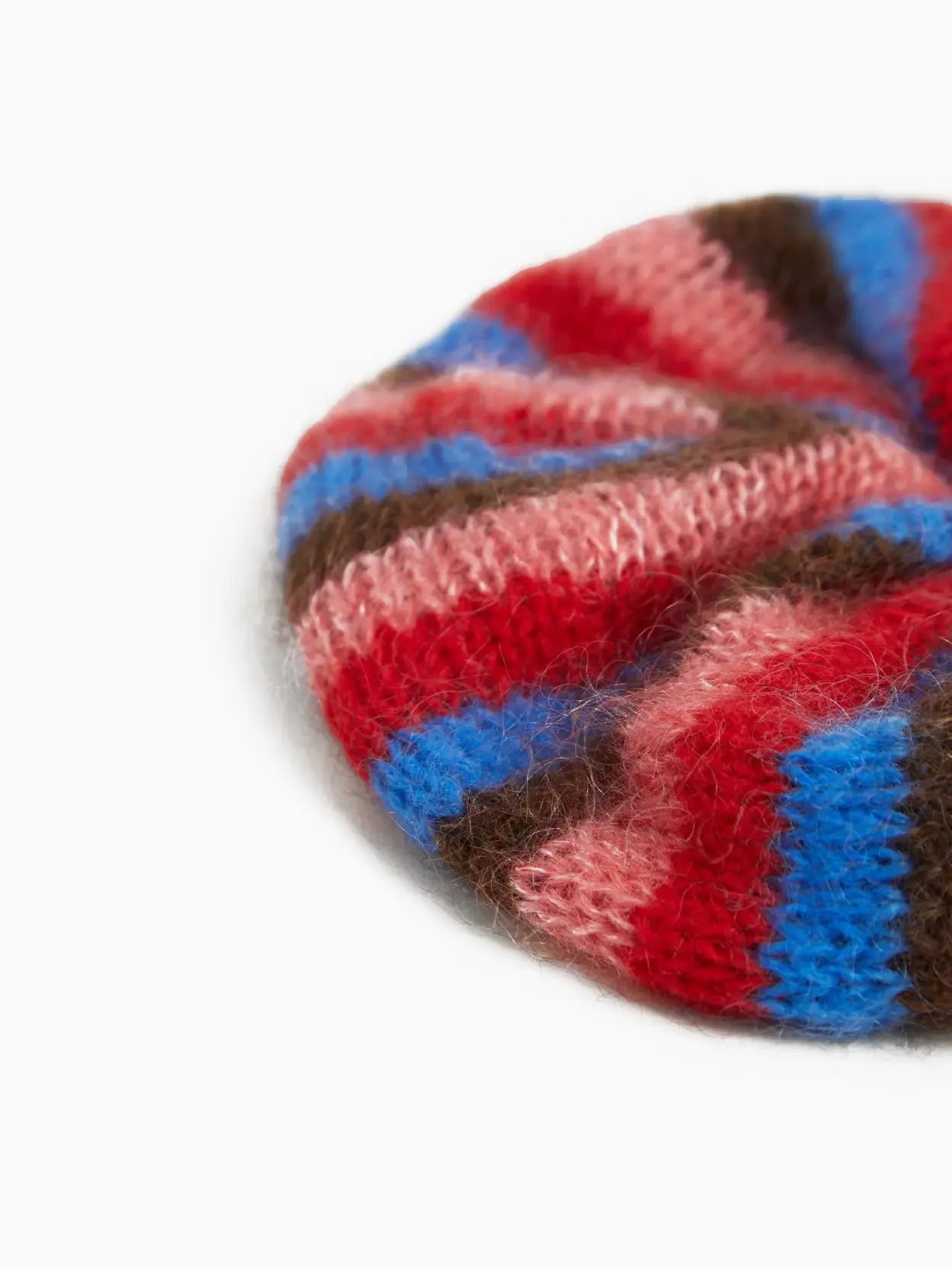 A round, knitted Mencia Scrunchie by Tomasa featuring alternating stripes of red, pink, blue, and brown. It has a small white label that reads "nanamica" sewn onto one of the red stripes. The scrunchie is displayed against a plain white background, available exclusively at Bassal Store in Barcelona.