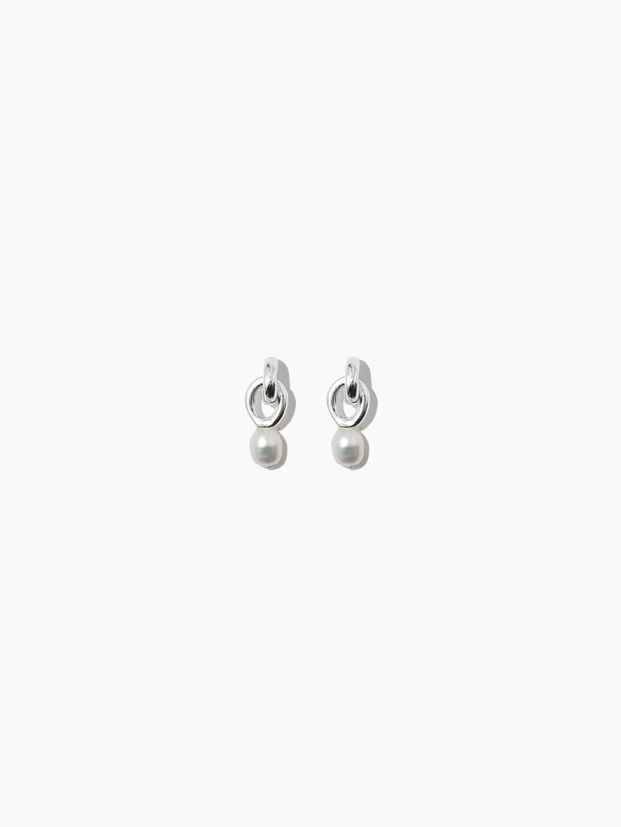A pair of Mini Sama Pearl Earrings from Nathalie Schreckenberg, featuring a small circular ring at the top and a spherical pearl hanging from each earring. The design is minimalist and sophisticated, echoing Barcelona's timeless style. The background is white.
