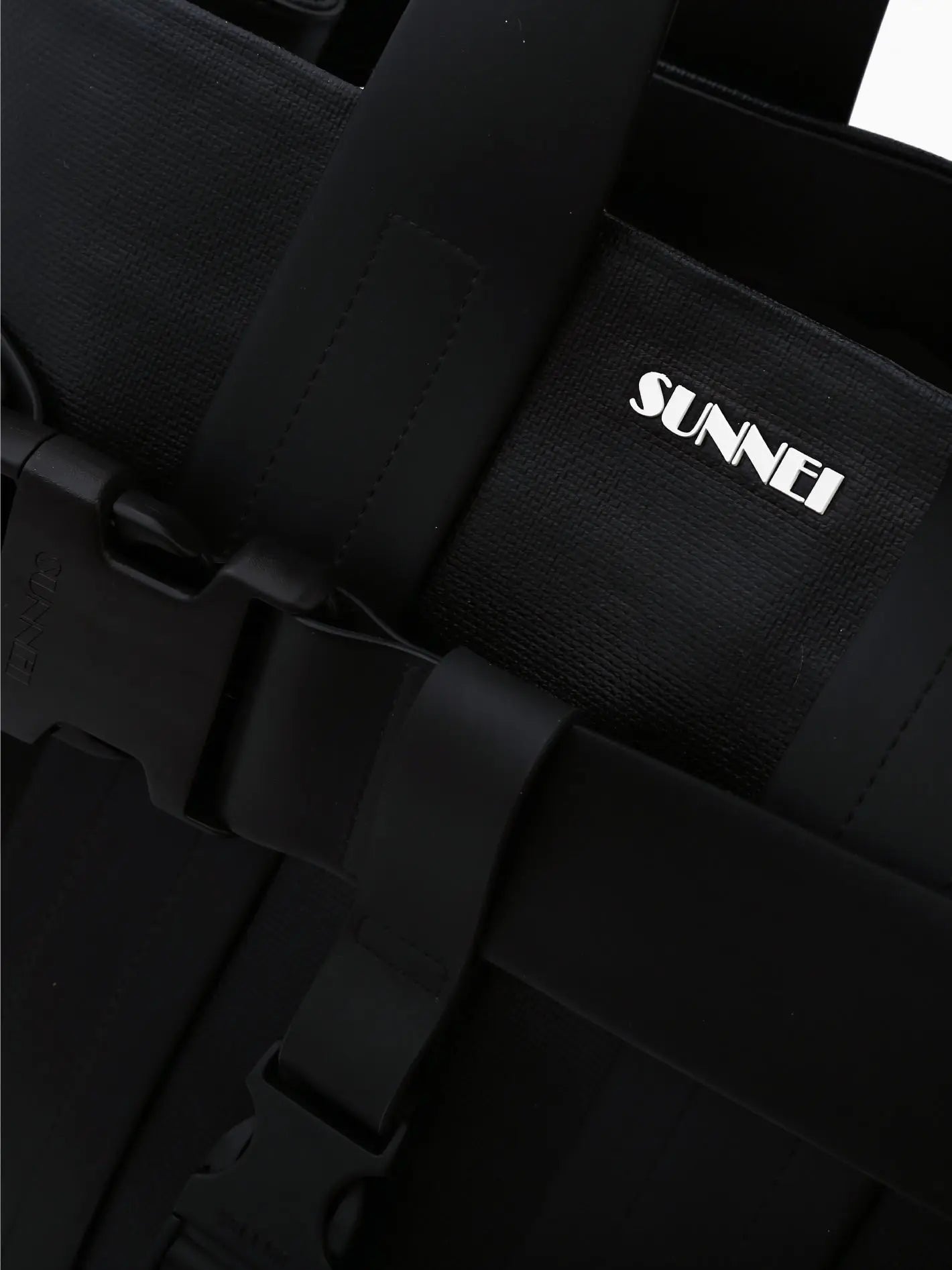A sleek black Parallelepipedo Messenger Bag Black with wide handles and a decorative strap featuring a buckle across the front. The bag has a modern design with a subtle label displaying the brand name "Sunnei". Available exclusively at BassalStore in Barcelona, the plain white background emphasizes its minimalist aesthetic.
