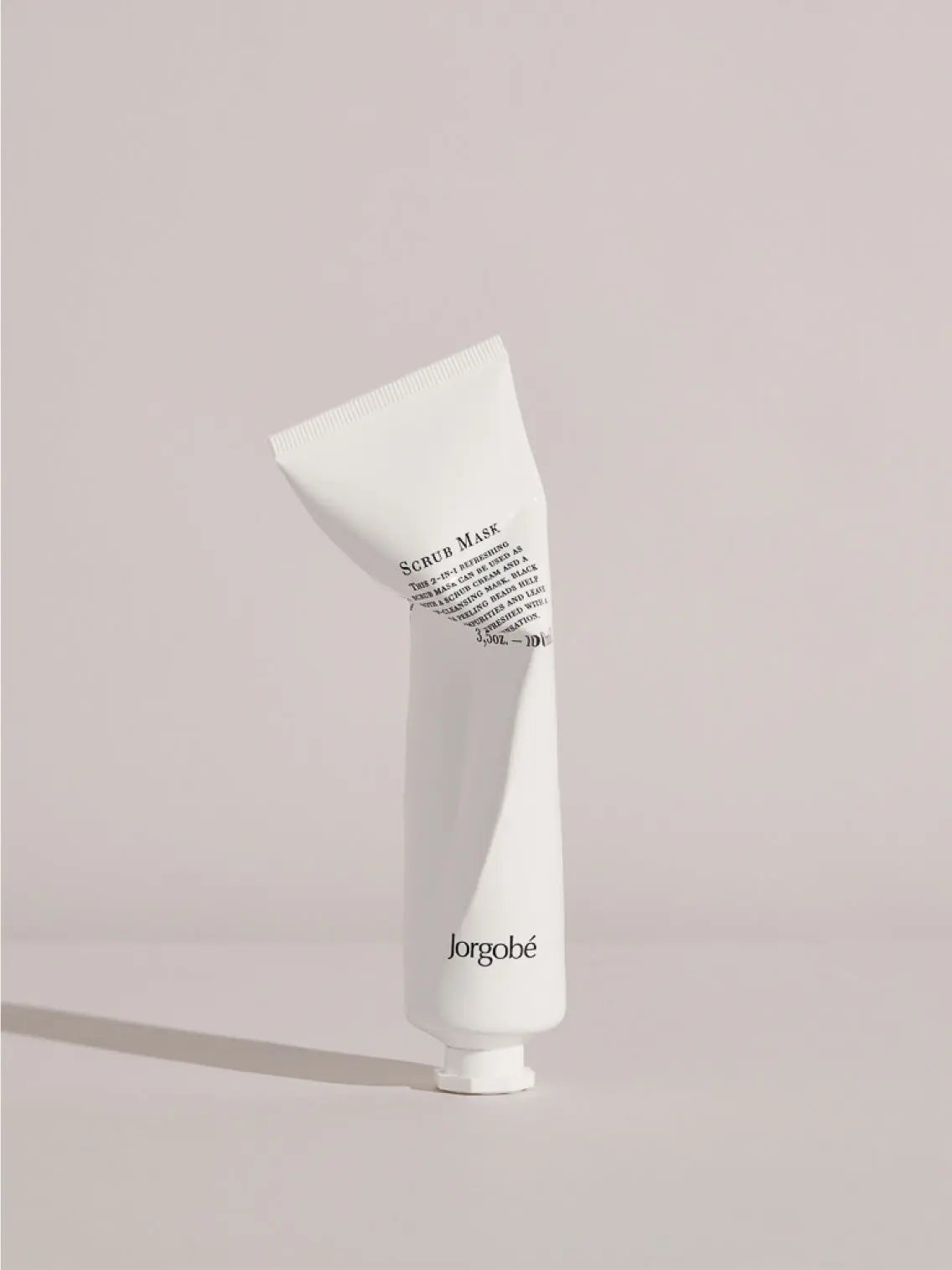 A white tube of Jorgobé Refreshing Scrub Mask 100ml stands next to its matching white and black polka-dotted box. Both the tube and the box display product information and volume (3.4 oz./100 ml). The tube has a white flip-top cap and is available at Bassalstore in Barcelona.