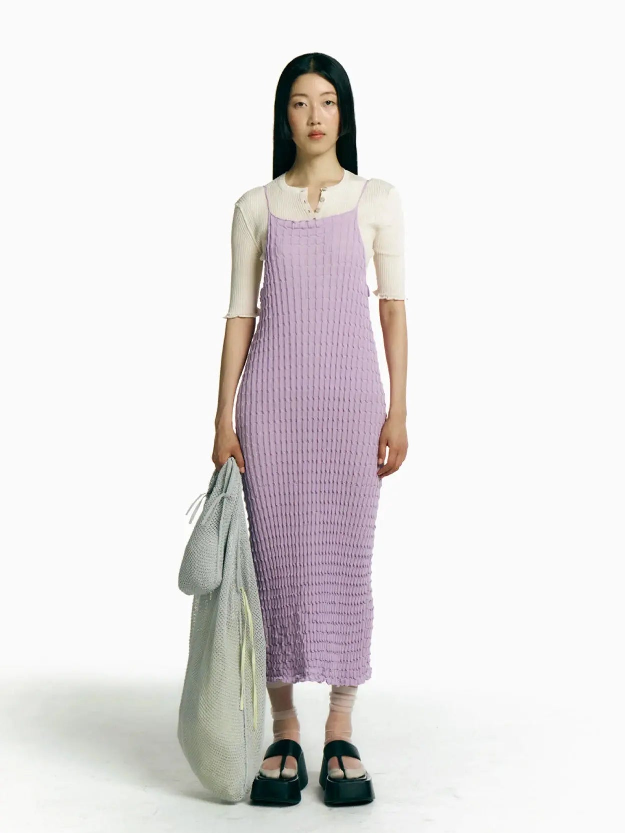 A Rina Dress Pink from Rus featuring a unique textured pattern with intricate, scalloped detailing. The dress has thin spaghetti straps and a long, flowing hem, giving it a stylish and elegant appearance perfect for exploring the streets of Barcelona.