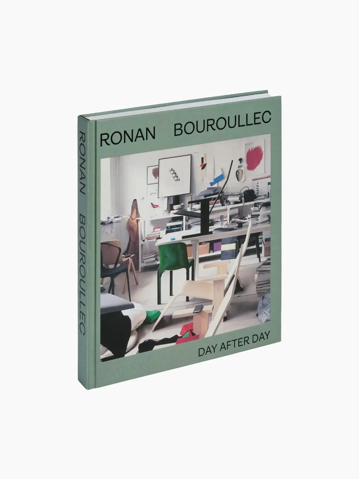 A green hardcover book titled "Ronan Bouroullec: Day After Day," available at Bassal Store in Barcelona, features a photograph of a cluttered studio with workstations, chairs, and art supplies on the cover. The author's name is printed in uppercase along the top and spine. This book is published by Phaidon.