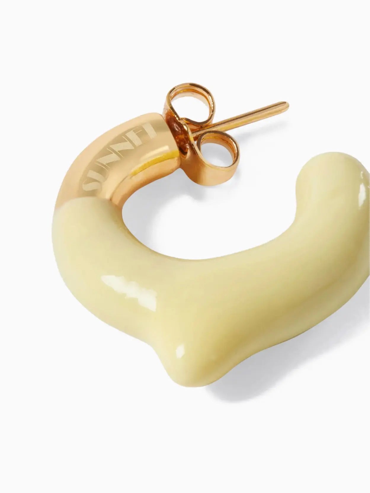 A pair of contemporary Rubberized Small Earrings by Sunnei featuring a unique, smooth, abstract shape. The earrings have a gold-toned attachment with a yellowish, irregularly curved resin design, giving them a modern and artistic appearance. Available at BassalStore in Barcelona. The background is plain white.