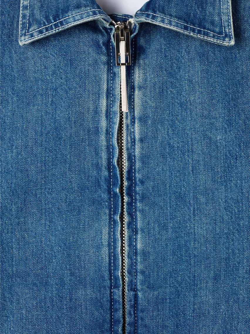 A light blue, organic bomber jacket made from raw denim, featuring a front zipper and long sleeves. The jacket includes a collar and two front pockets, exuding a casual, slightly faded look. A silicon Sunnei patch adds a unique touch, while the fabric tag inside the collar reads "Marni.