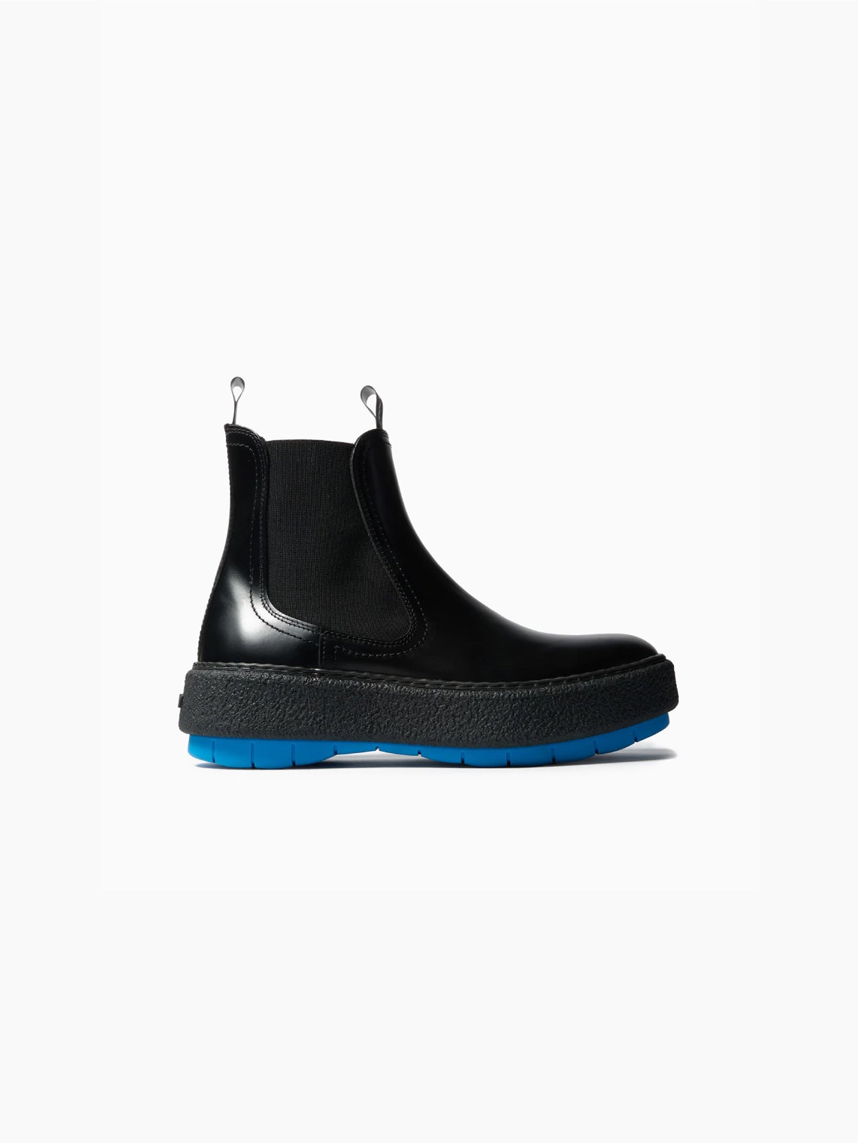 The Cemento Chelsea Boot by Sunnei is a black leather ankle boot with a chunky textured sole. It features black detailing and a vibrant blue tread, along with elastic side panels and pull tabs for easy wear, all set against a plain white background.