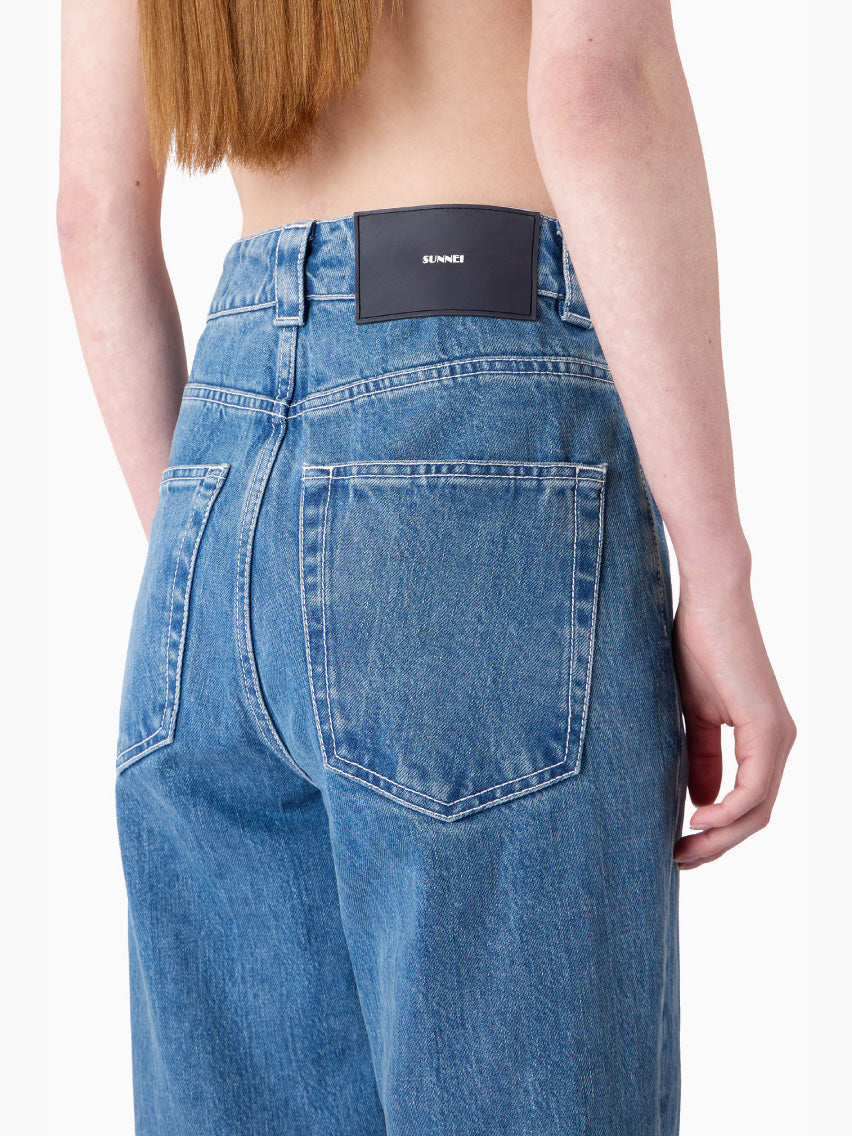 A pair of Sunnei Classic Denim Pants Washed Blue, featuring a high-waisted, straight-leg design made from organic cotton with a classic five-pocket arrangement and secured with a zip fly and button closure, laid flat on a white background.