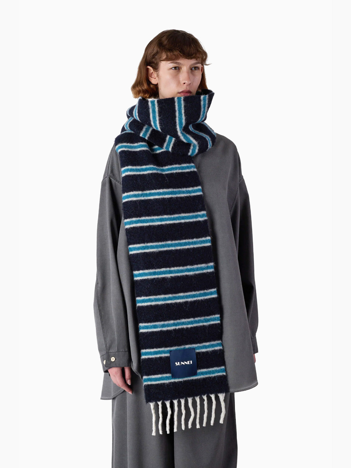 Introducing the Blue Stripes Scarf by Sunnei, a folded accessory with horizontal lines in black, blue, and white. Crafted from luxurious alpaca wool, it is elegantly accented with fringes at the ends and features a small rectangular label.