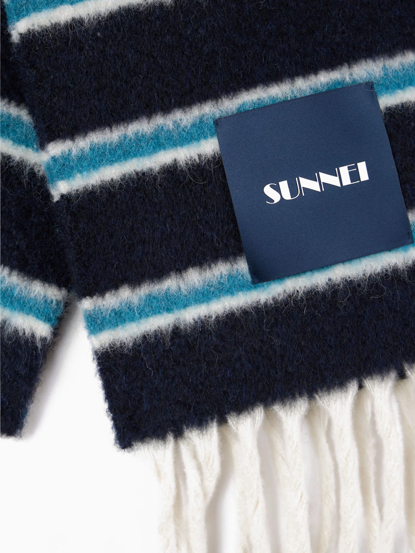 Introducing the Blue Stripes Scarf by Sunnei, a folded accessory with horizontal lines in black, blue, and white. Crafted from luxurious alpaca wool, it is elegantly accented with fringes at the ends and features a small rectangular label.