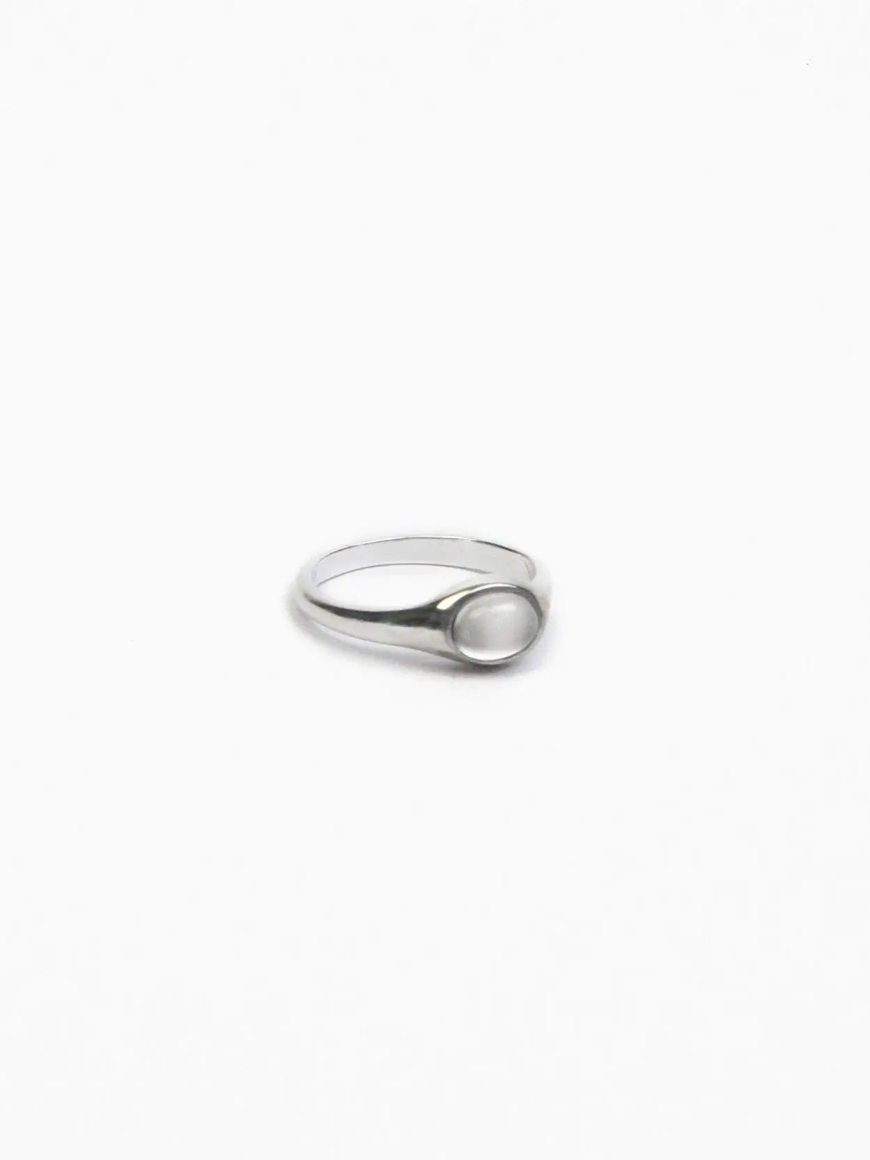 A minimalist silver ring with a smooth, oval-shaped white stone set in the center against a plain white background. The band is slender and simplistic, complementing the elegant and understated design of the Single Stone Ring by Nathalie Schreckenberg available at BassalStore in Barcelona.