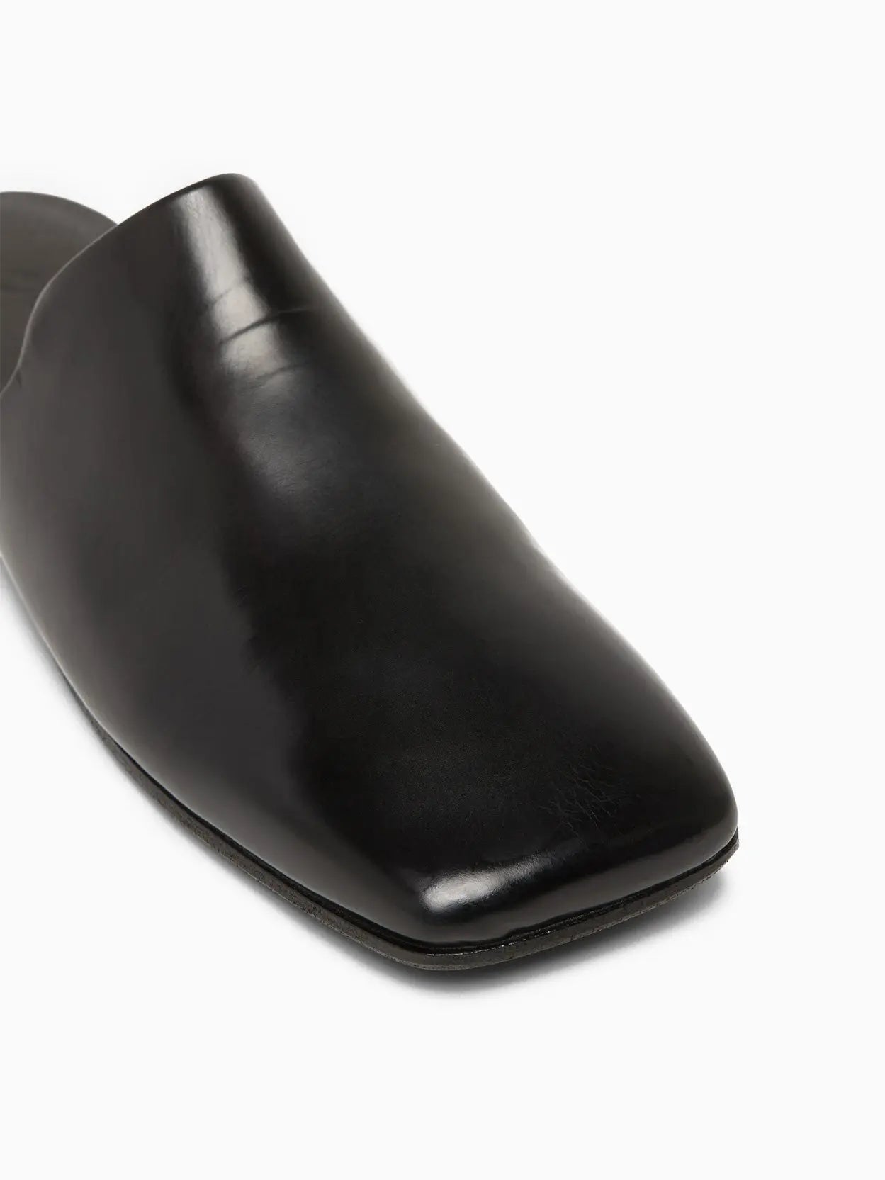 A sleek black leather mule slipper with a flat sole, open back, and round toe design on a white background. Available at Bassalstore in Barcelona, the Spatolona Mule Black by Marsèll features a smooth, polished finish and a low-profile silhouette.