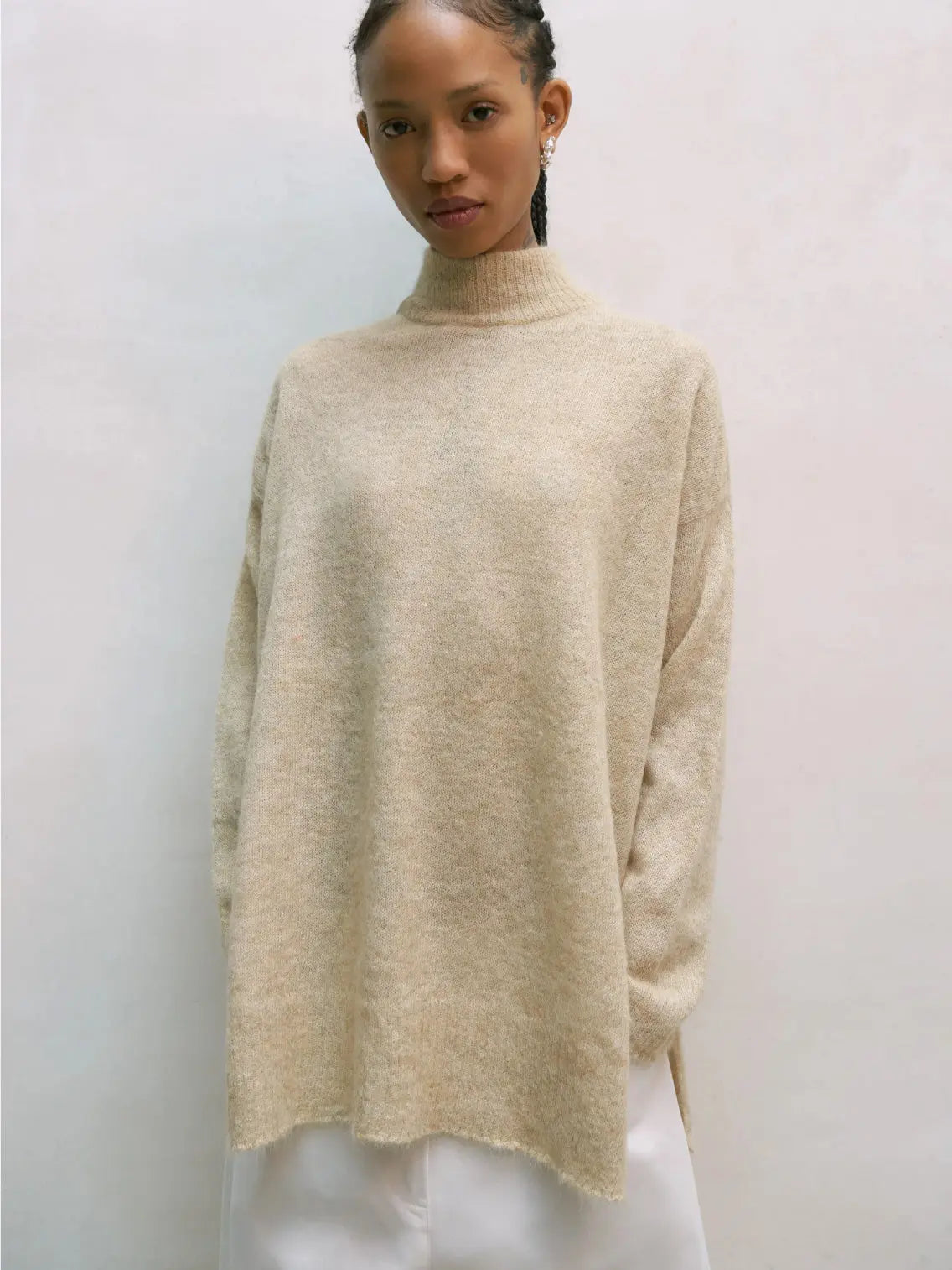 A beige, long-sleeved, knitted Suri Turtleneck Sweater Avene from Cordera. The sweater has a loose, relaxed fit and appears to be made of soft, cozy material. It is laid flat against a plain white background.