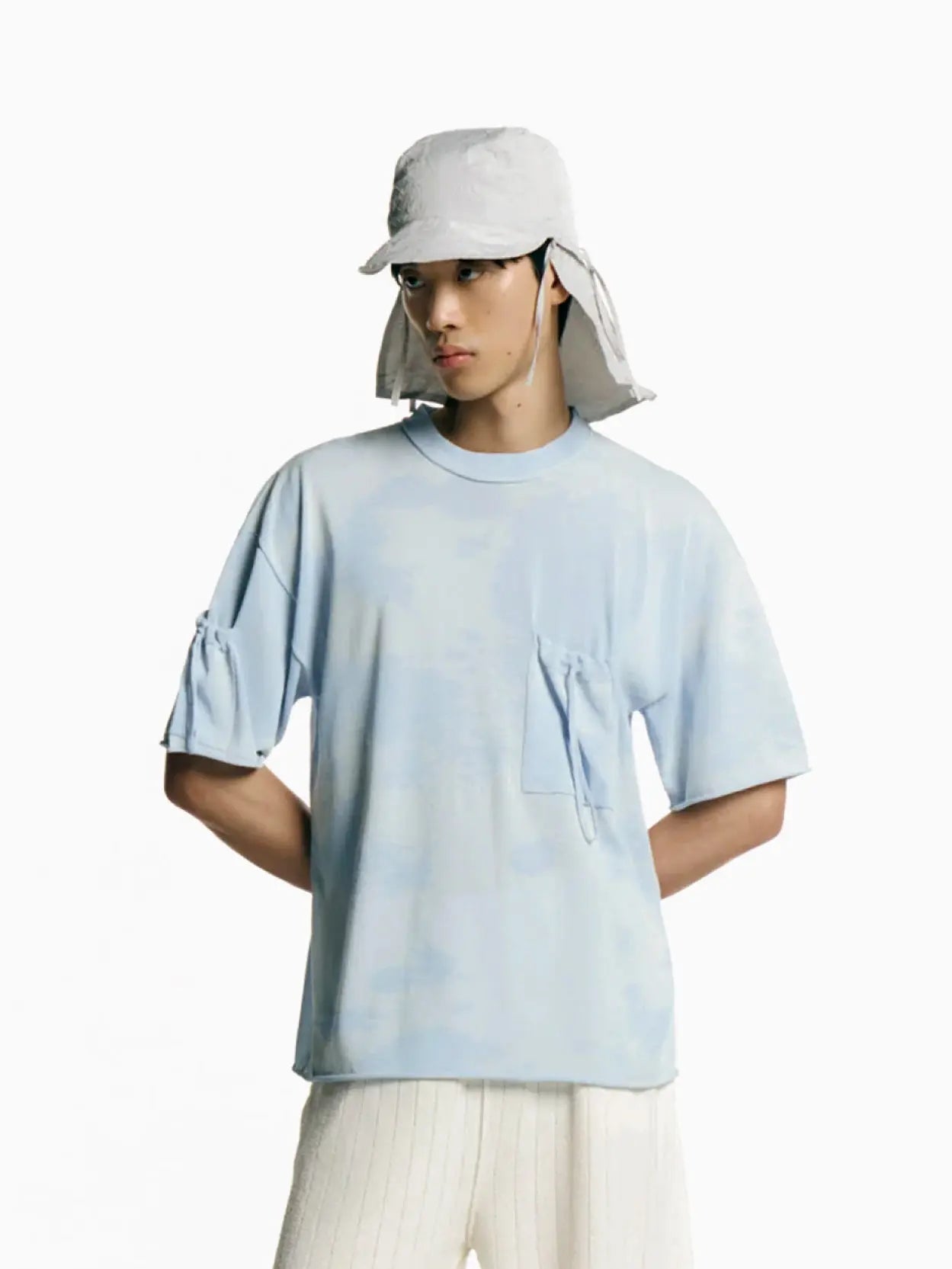 Person with short black hair wearing a Tako Cap Ice Grey by Rus, with long side flaps and a dark-colored collared shirt. This stylish look could easily be found at a trendy store in Barcelona. The background is plain white.
