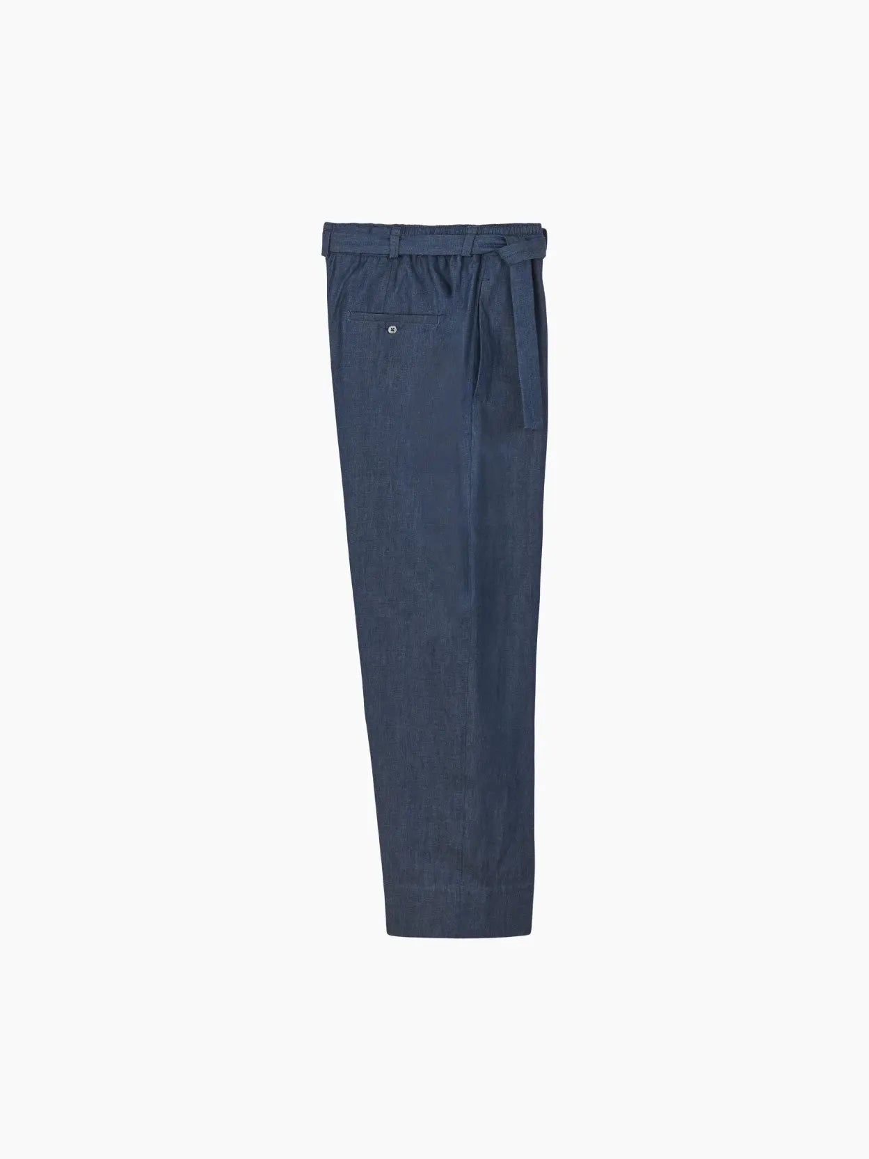 A pair of loose-fit, high-waisted navy blue trousers made from a lightweight fabric. The trousers feature a drawstring waistband and a single back pocket with a button closure. This stylish piece, Taurus Pants Denim by Jan Machenhauer, is available at the Bassal Store in Barcelona, shown from the side on a plain white background.