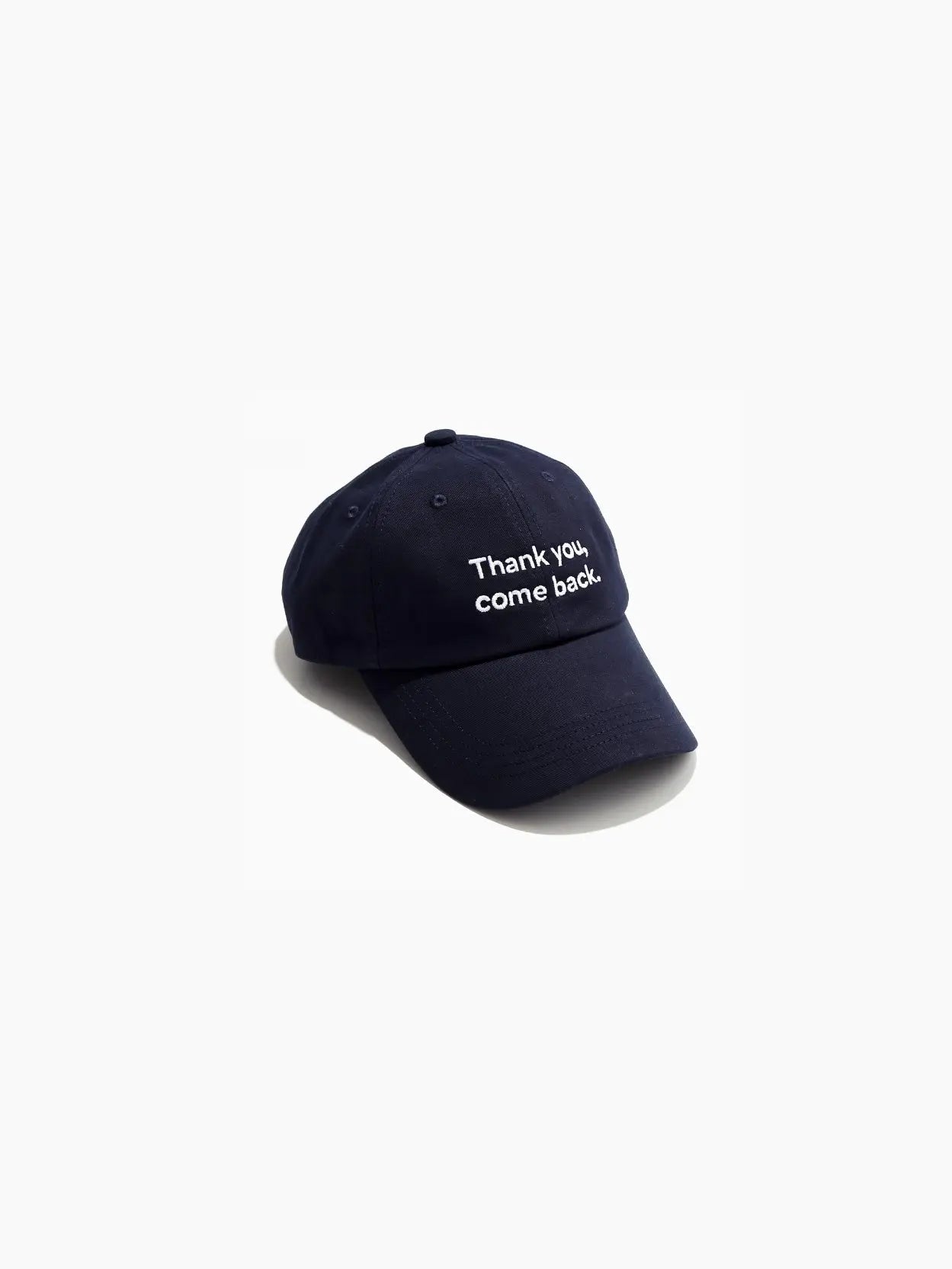 A Thank You, Come Back Cap Navy from Bassal Store with the text "Thank you, come back." embroidered in white on the front. The cap has a curved brim and six panels with stitching details. Perfect for your next visit to a bustling store in Barcelona.