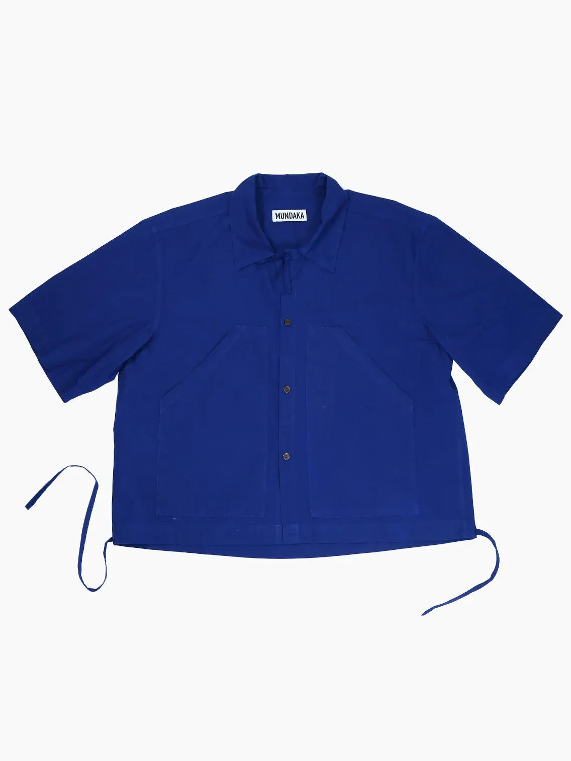 A Boxy Shirt Navy with a relaxed fit. It features a pointed collar, two large front pockets, and drawstrings at the side hems. The brand label "Mundaka" is visible inside the collar. Available now at Bassal Store in Barcelona.