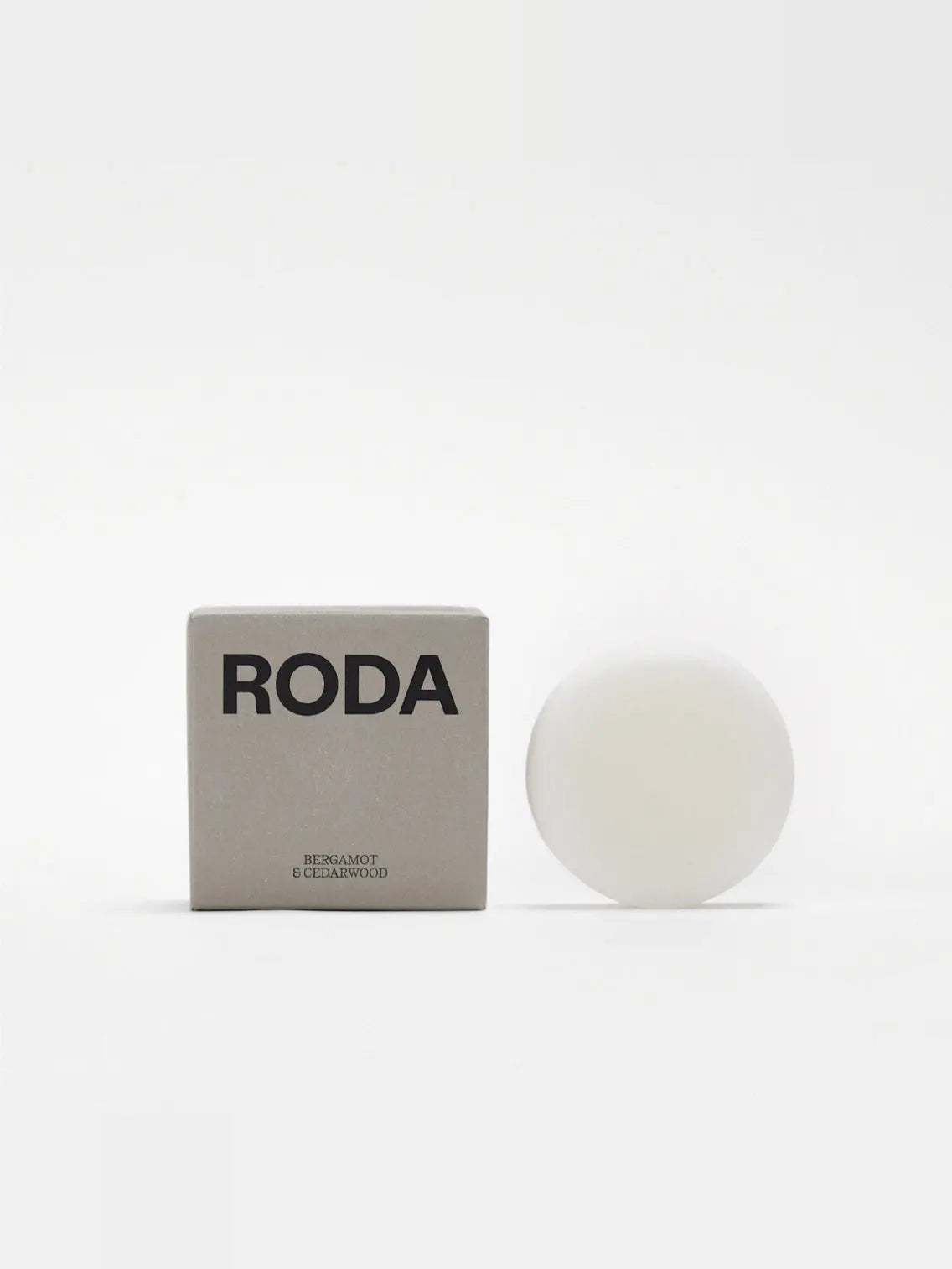 A round white conditioner bar sits next to a beige and gray box labeled "Roda," available exclusively at Bassalstore. Text on the box reads "Bergamot & Cedarwood." The background is plain white.