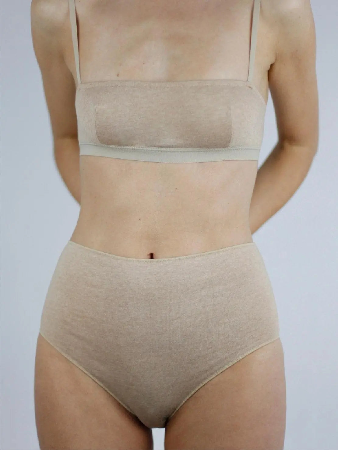 A person wearing a matching beige bra and Earth Basic Highwaist Organic Cotton Briefs from Talk Under Light stands against a plain white background. The focus is on the person's torso, highlighting the comfortable and seamless fit of the undergarments available at this trendy store in Barcelona.