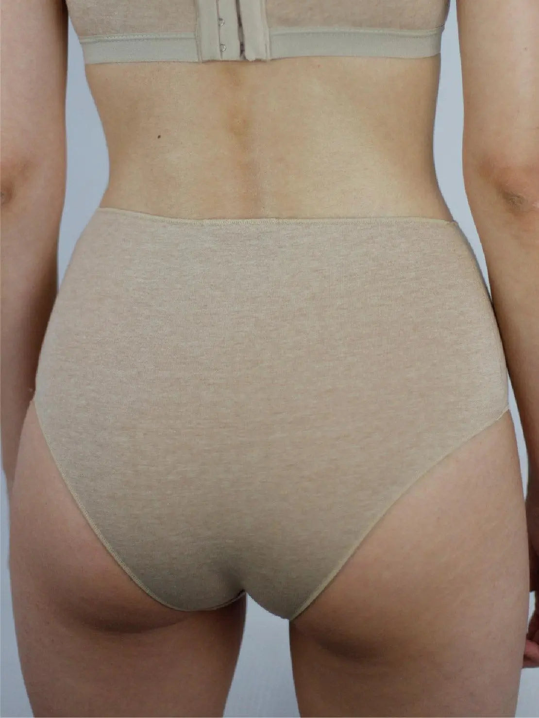 A person wearing a matching beige bra and Earth Basic Highwaist Organic Cotton Briefs from Talk Under Light stands against a plain white background. The focus is on the person's torso, highlighting the comfortable and seamless fit of the undergarments available at this trendy store in Barcelona.