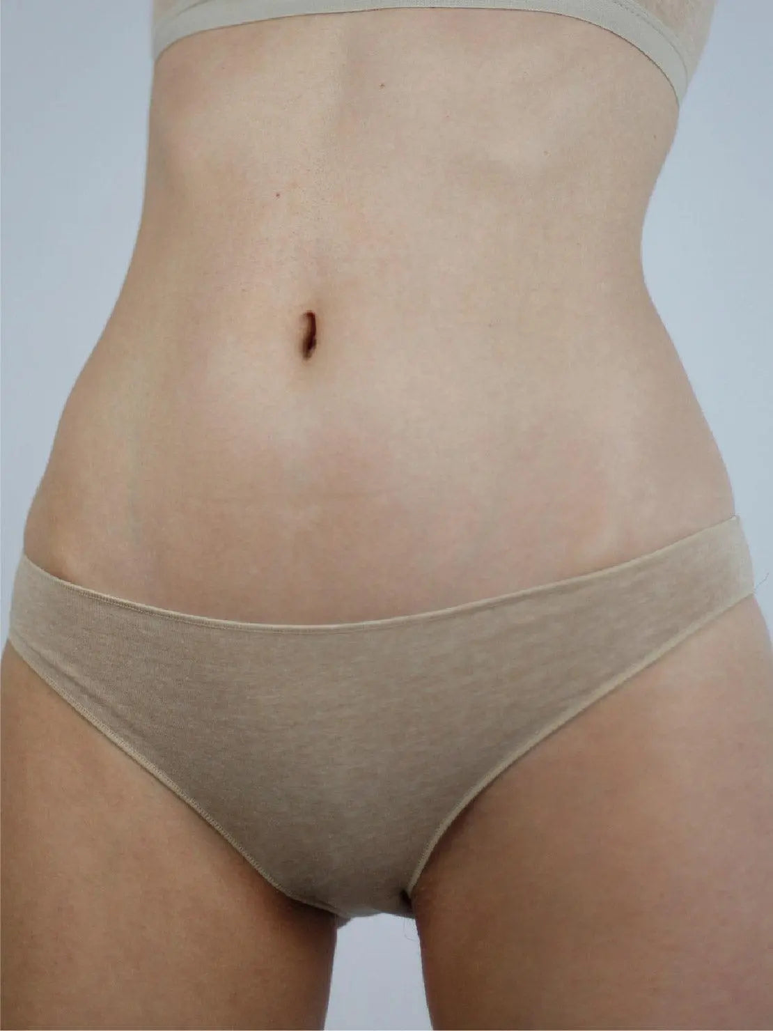 Close-up of a person wearing Earth Classic Organic Cotton Briefs - Talk Under Light and a matching crop top from Bassalstore, focusing on the midsection and lower torso. The background is plain and light-colored.
