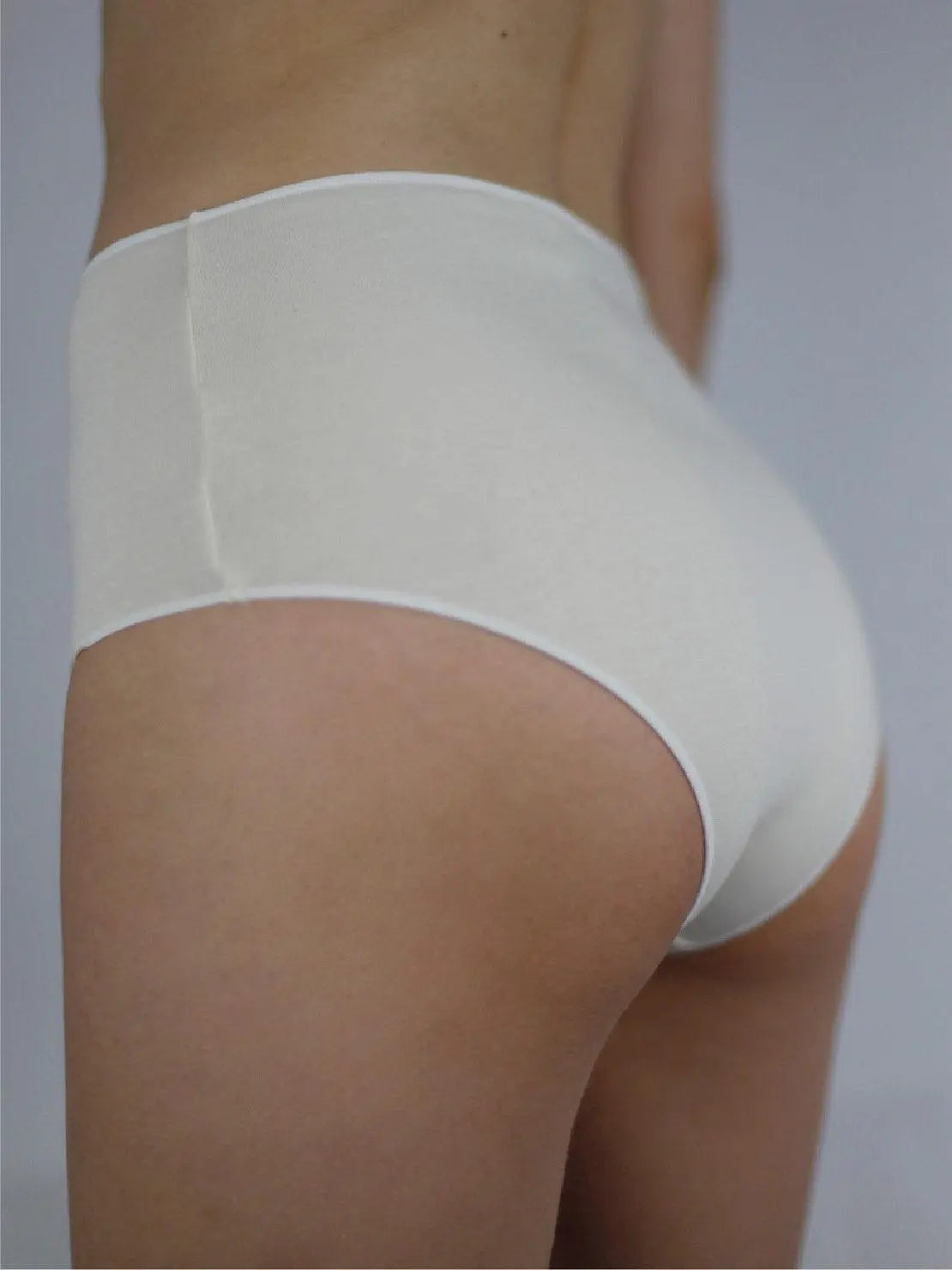 A person is shown from the torso down wearing Ecru Basic Highwaist Organic Cotton Briefs - Talk Under Light and a banded white bralette. The background is neutral, focusing attention on the minimalist undergarments available at Bassalstore in Barcelona.