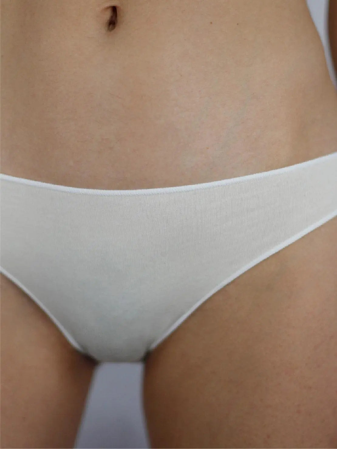 A person wearing white underwear and a white top from Talk Under Light is standing against a plain background. The focus is on the midsection, showcasing the fit and style of the Ecru Classic Organic Cotton Briefs - Talk Under Light available at this Barcelona-based store.