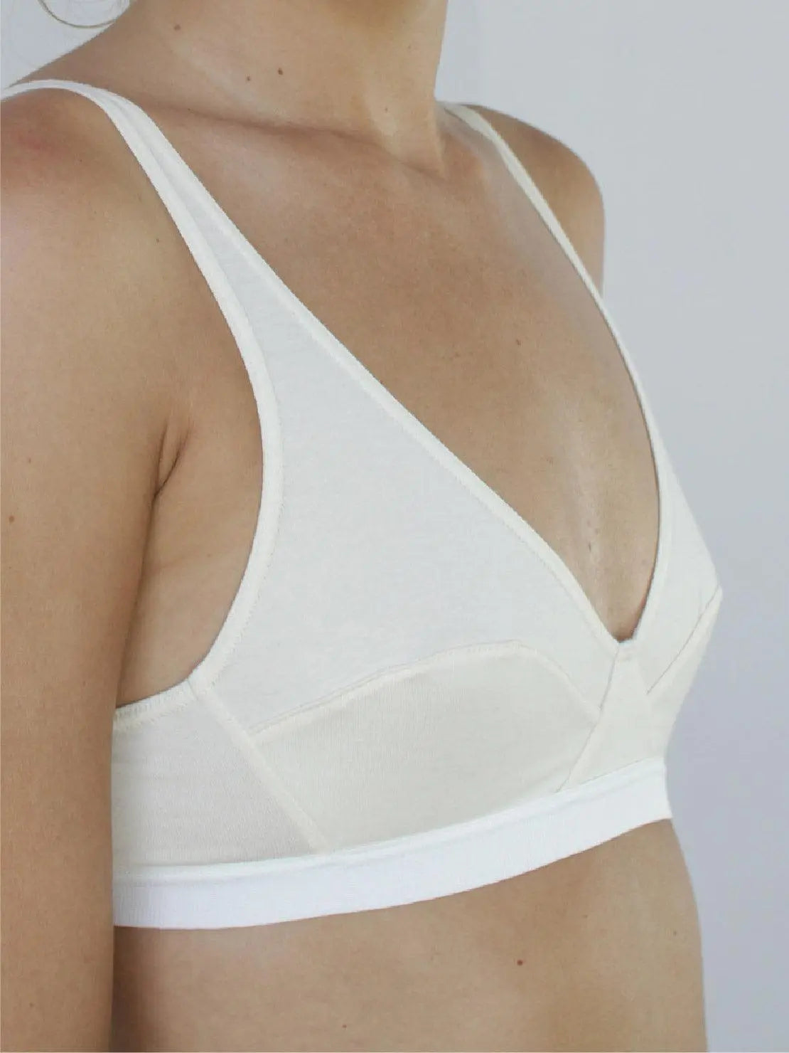 Close-up of a person wearing an Ecru Mia Organic Cotton Bra with thin straps from Talk Under Light. The bra features a deep V-neck design and a wide elastic band under the bust for support. The image captures the upper torso against a plain, light background, reminiscent of Barcelona's effortless style.