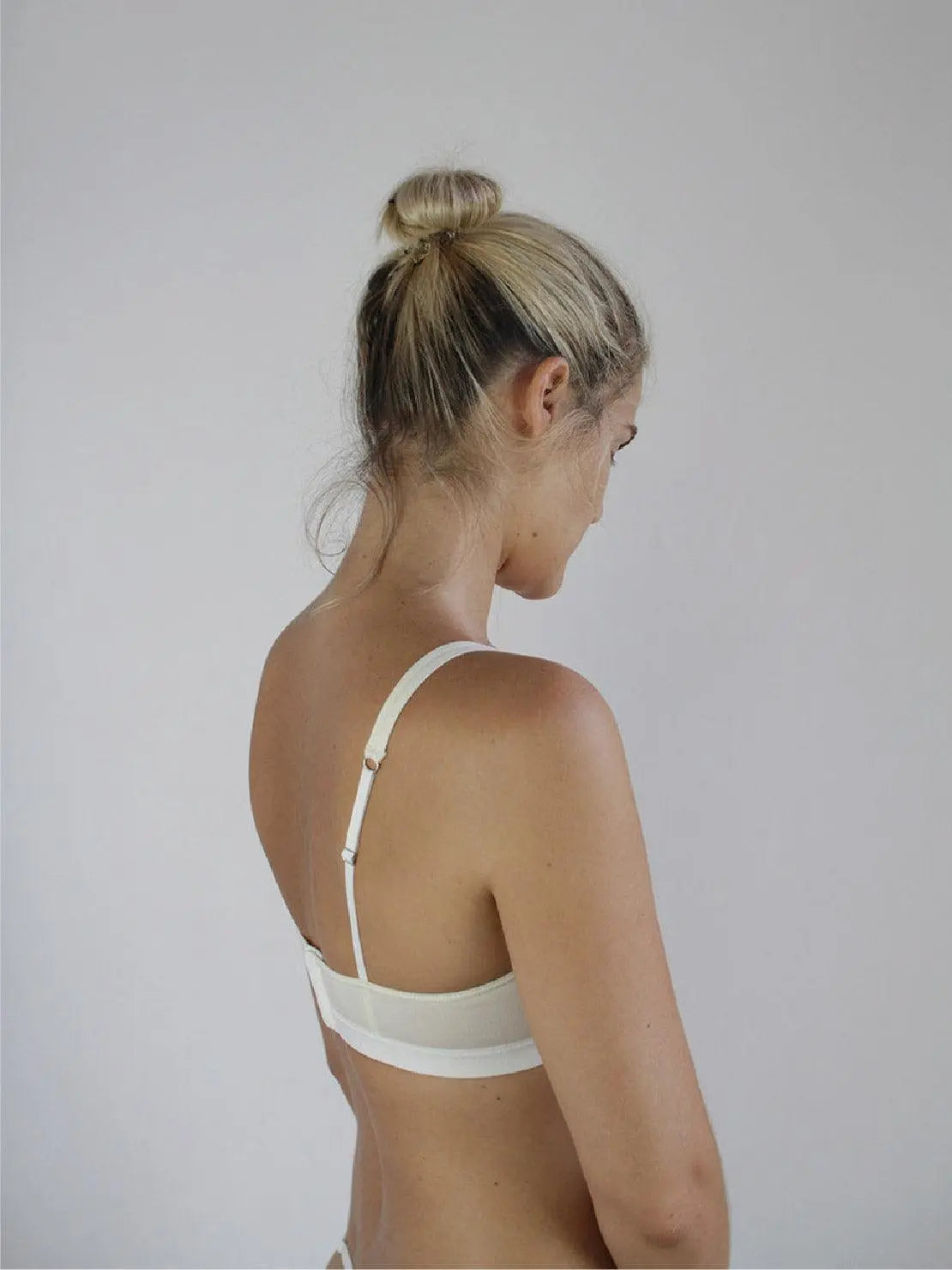Close-up of a person wearing an Ecru Mia Organic Cotton Bra with thin straps from Talk Under Light. The bra features a deep V-neck design and a wide elastic band under the bust for support. The image captures the upper torso against a plain, light background, reminiscent of Barcelona's effortless style.